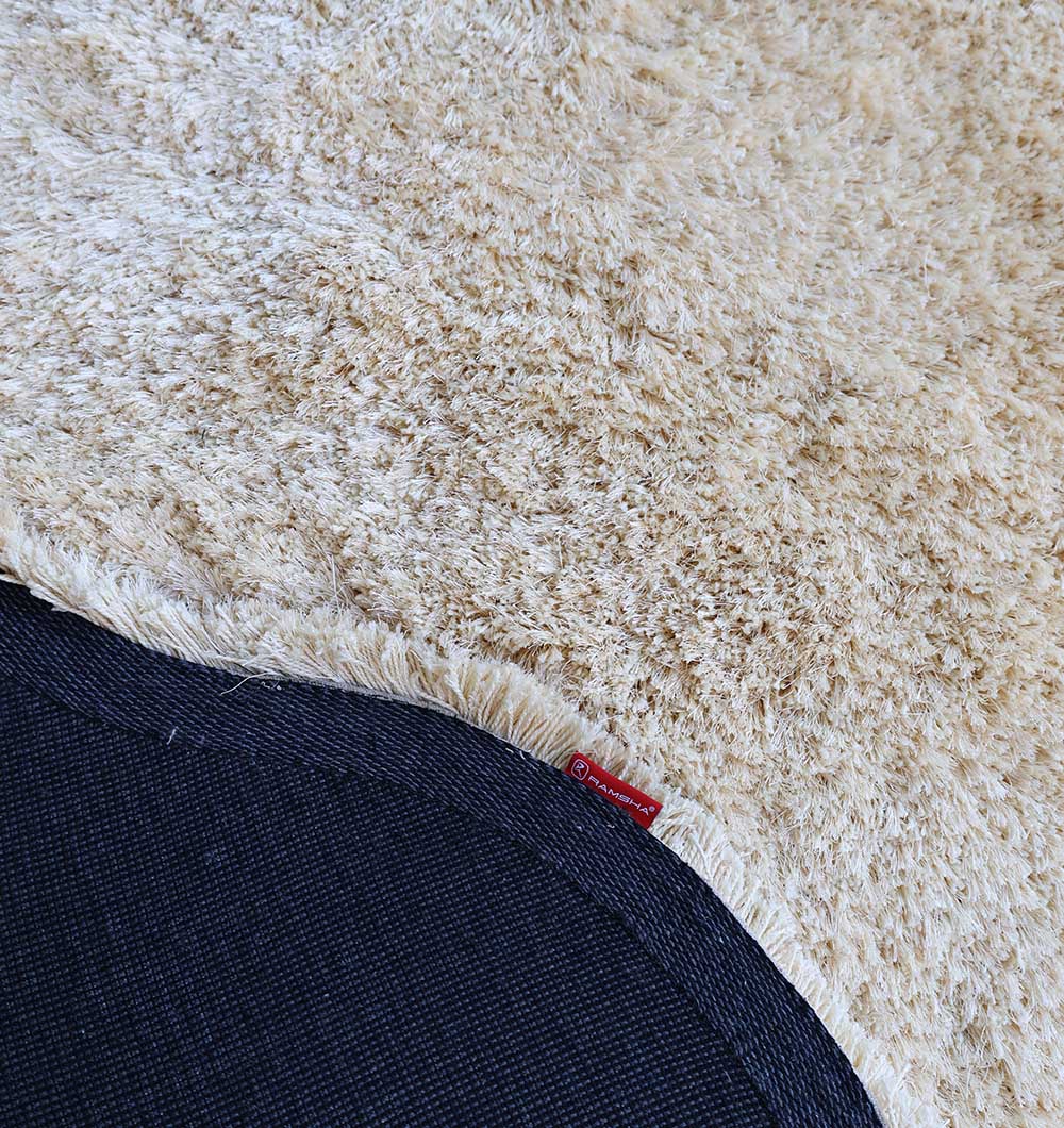 A close-up of the RAMSHA HOME Shaggy Rug for Living Room - SG 026 showcases its ivory shag pile, black fabric backing partially visible, and a small red tag sewn near the edge.