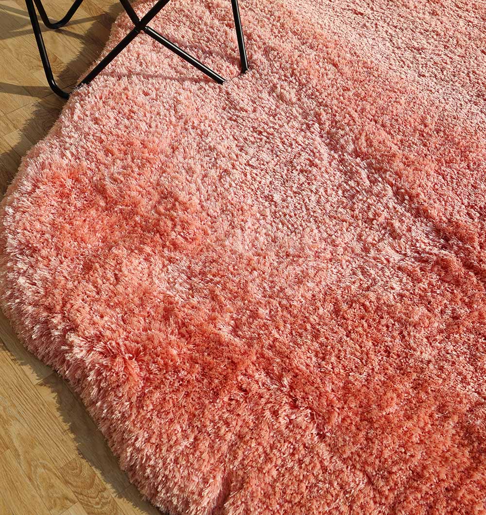A close-up of the RAMSHA HOME Shaggy Shape Rug for Living Room - SG 027-B (200x300 cm) in plush pink rests on a light wooden floor, with black metal chair legs visible in the upper left corner.
