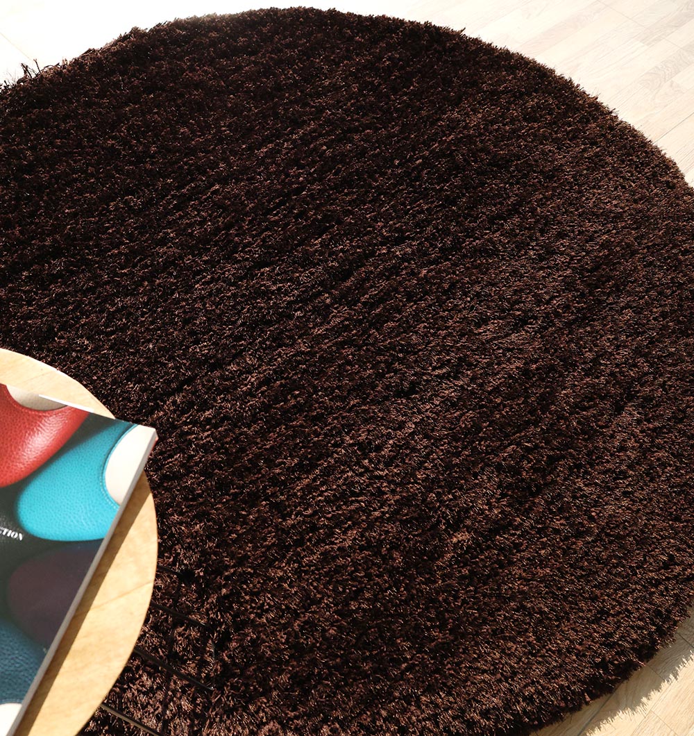 The RAMSHA HOME Dark Brown High-Density Shaggy Rug - SG 028 adds coziness to a light wooden floor, with a small table and colorful book peeking in from the lower left corner.