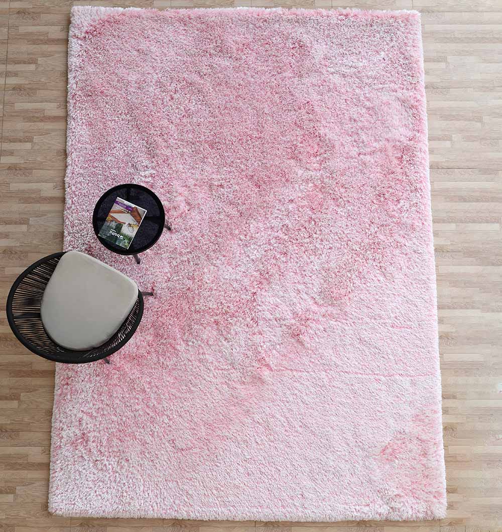 The RAMSHA HOME Light Pink Color Dining Room Shaggy Rug - SG 02 lies on a light wood floor, topped in one corner by a round black side table with a magazine and a modern chair with a light cushion.
