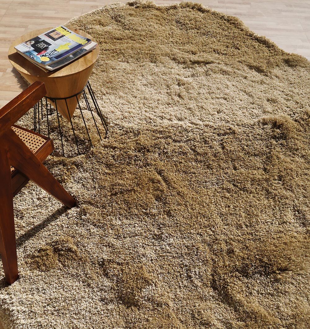 The RAMSHA HOME Large Beige Shaggy Shape Rug for Living Room - SG 030 (200x300 cm) lies on a tiled floor, with a wooden chair featuring a woven seat to the left and a small wooden side table topped with magazines nearby.