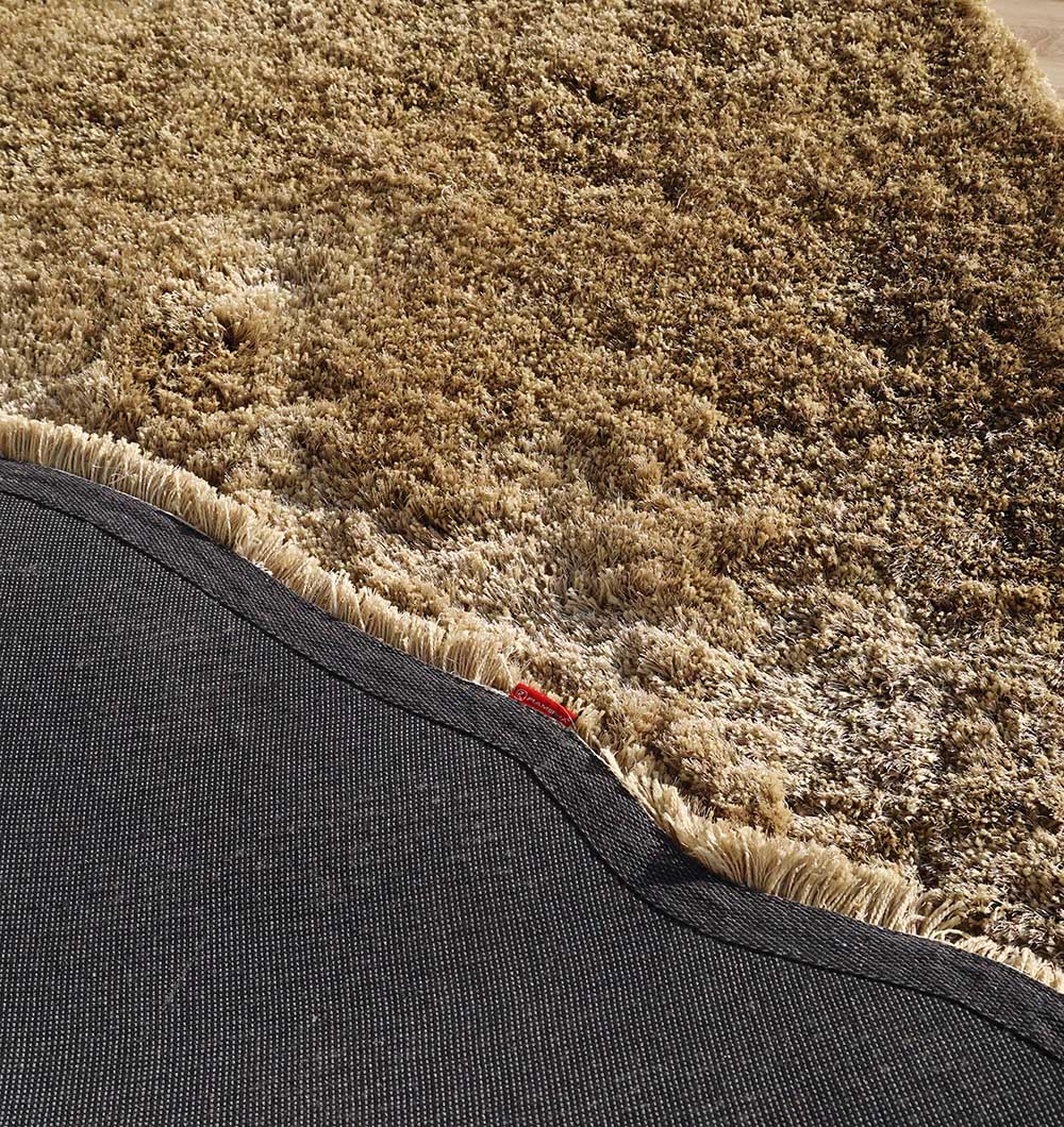 Close-up of the RAMSHA HOME Large Beige Shaggy Shape Rug (SG 030, 200x300 cm) for living rooms, featuring a thick pile, beige fringe on the edge, and black non-slip backing. The rug is slightly folded to show both sides.