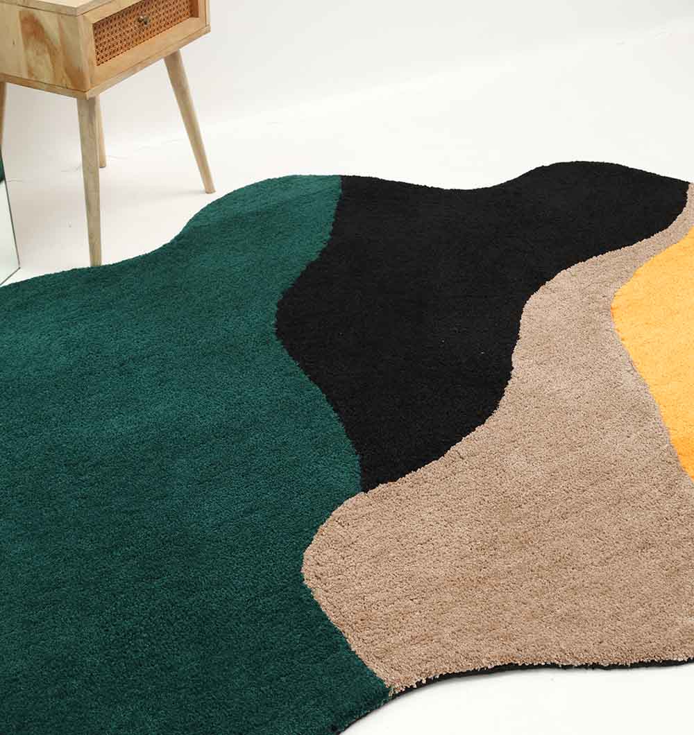 The RAMSHA HOME Shaggy Rug for Living Room - SG 036 (160x230 cm), featuring abstract wavy shapes in dark green, black, beige, and yellow, lies on a white floor beside a light wood table with a rattan drawer.
