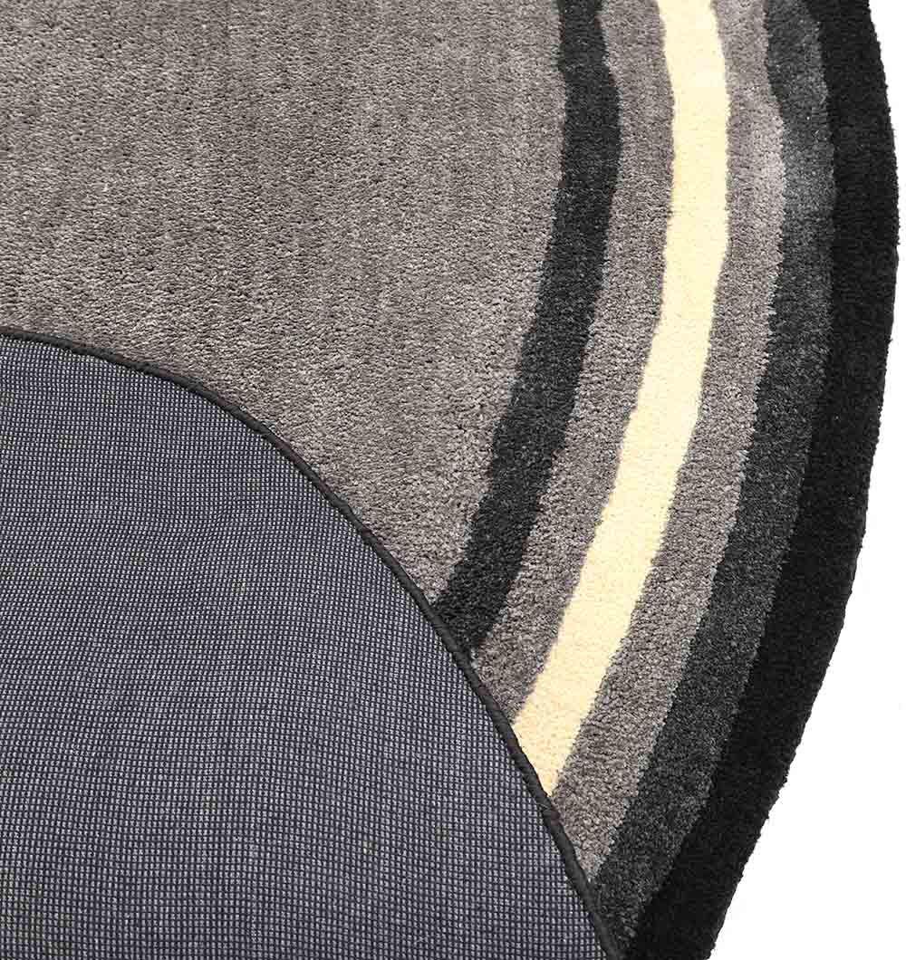 A close-up of two overlapping rugs: RAMSHA HOME's Shaggy Rug for Living Room - SG 037 (160X230 cm) with curved gray, black, and cream stripes alongside a plain gray fabric rug.