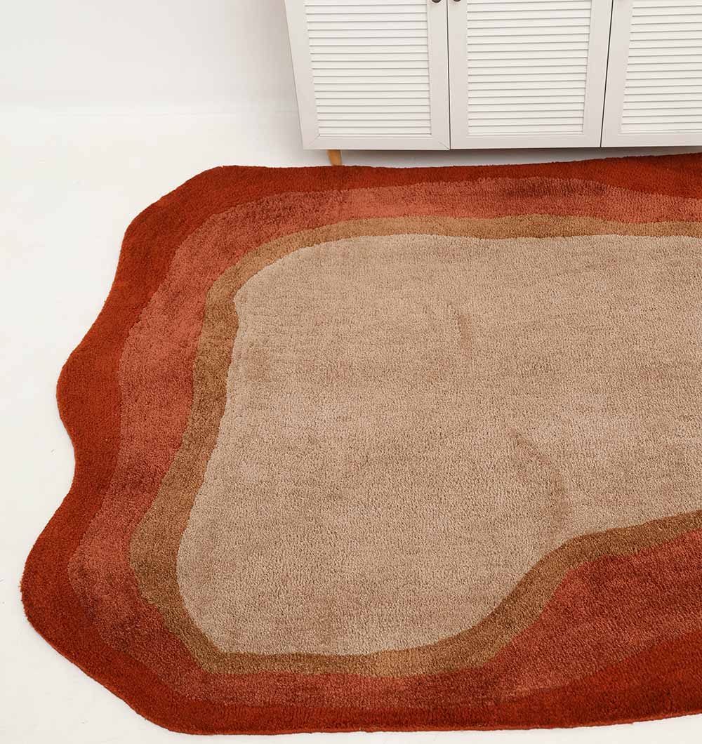 The RAMSHA HOME Shaggy Rug for Living Room - SG 038 (160x230 cm) features an irregular hand-tufted design with wavy edges and layered beige, brown, and rust hues, shown on a white floor beside a cabinet with shutter-style doors.