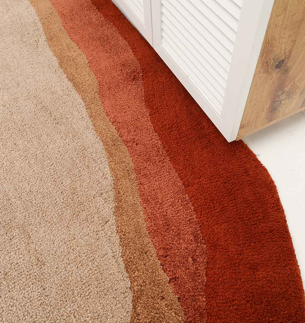 A close-up of the RAMSHA HOME Shaggy Rug for Living Room - SG 038 (160x230 cm) featuring beige, tan, brown, and rust wavy patterns, shown on the floor beside a white louvered cabinet with a wood-textured side.
