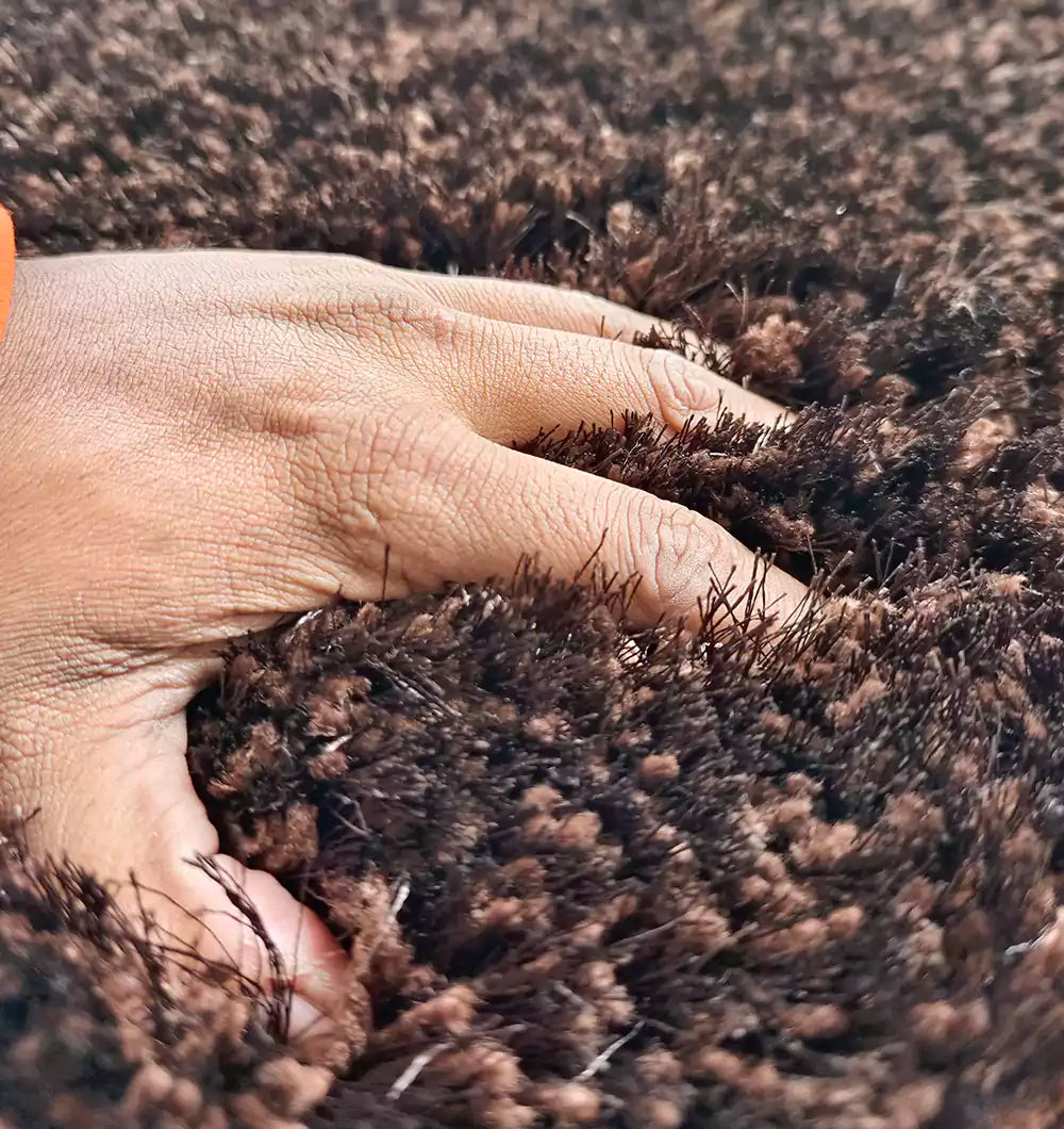 A close-up of a hand presses into the RAMSHA HOME Fluffy Shaggy Area Rug SG 04 in a brown rectangle, separating the thick fibers to reveal the rug’s rich texture.