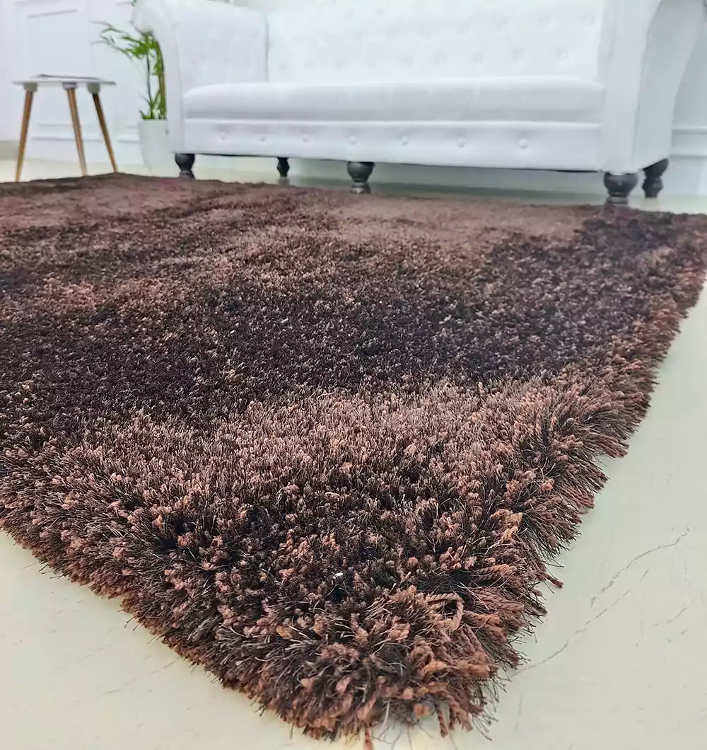A close-up of the RAMSHA HOME Fluffy Shaggy Area Rug SG 04 in brown, rectangle-shaped, placed on a light floor with a white sofa and small side table in the background.