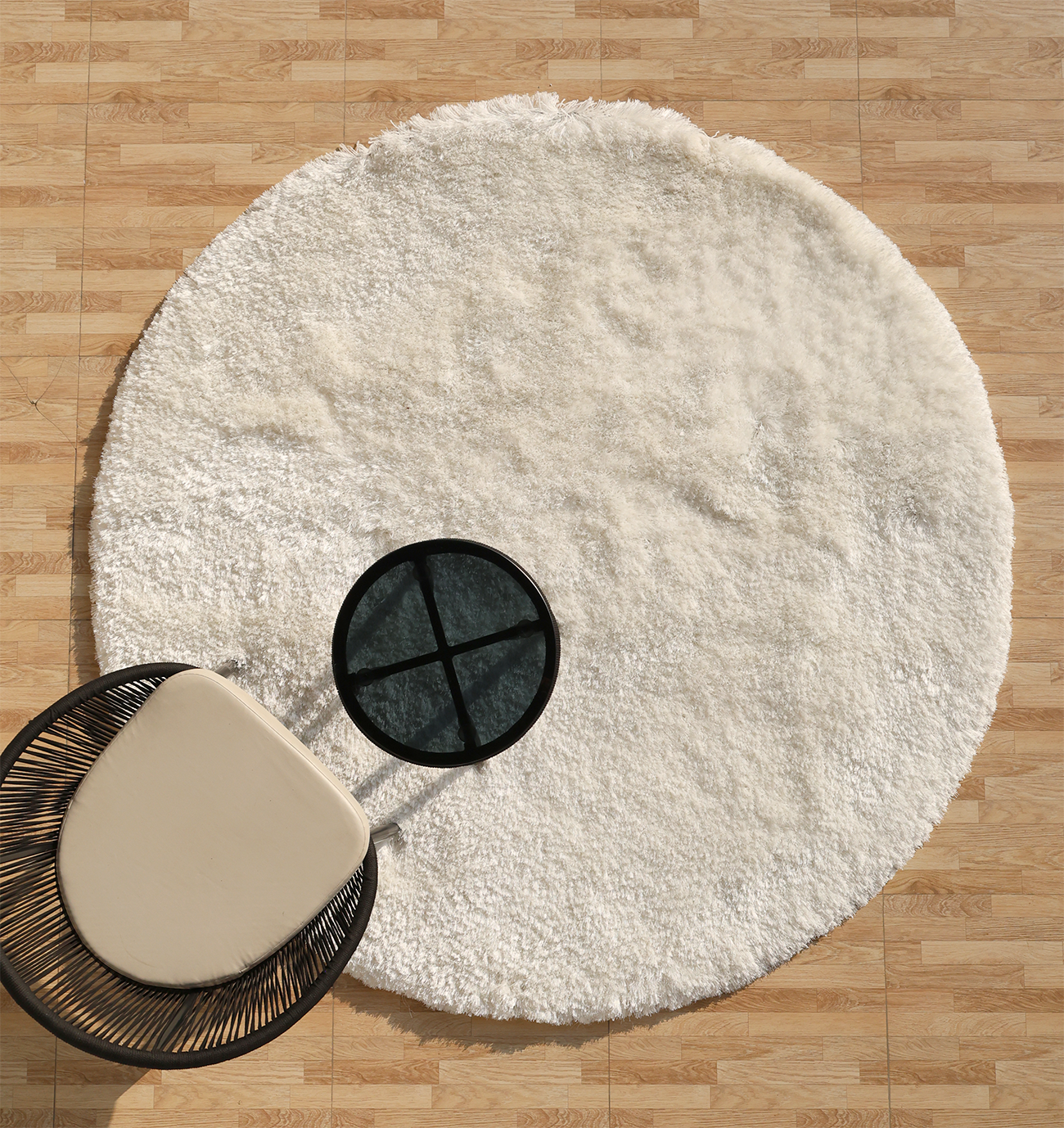 The RAMSHA HOME White Color Plush Shaggy Area Rug - SG 040 adds coziness to a light wood floor, paired with a modern black and beige chair and a small round black side table partly set on the soft, fluffy rug.