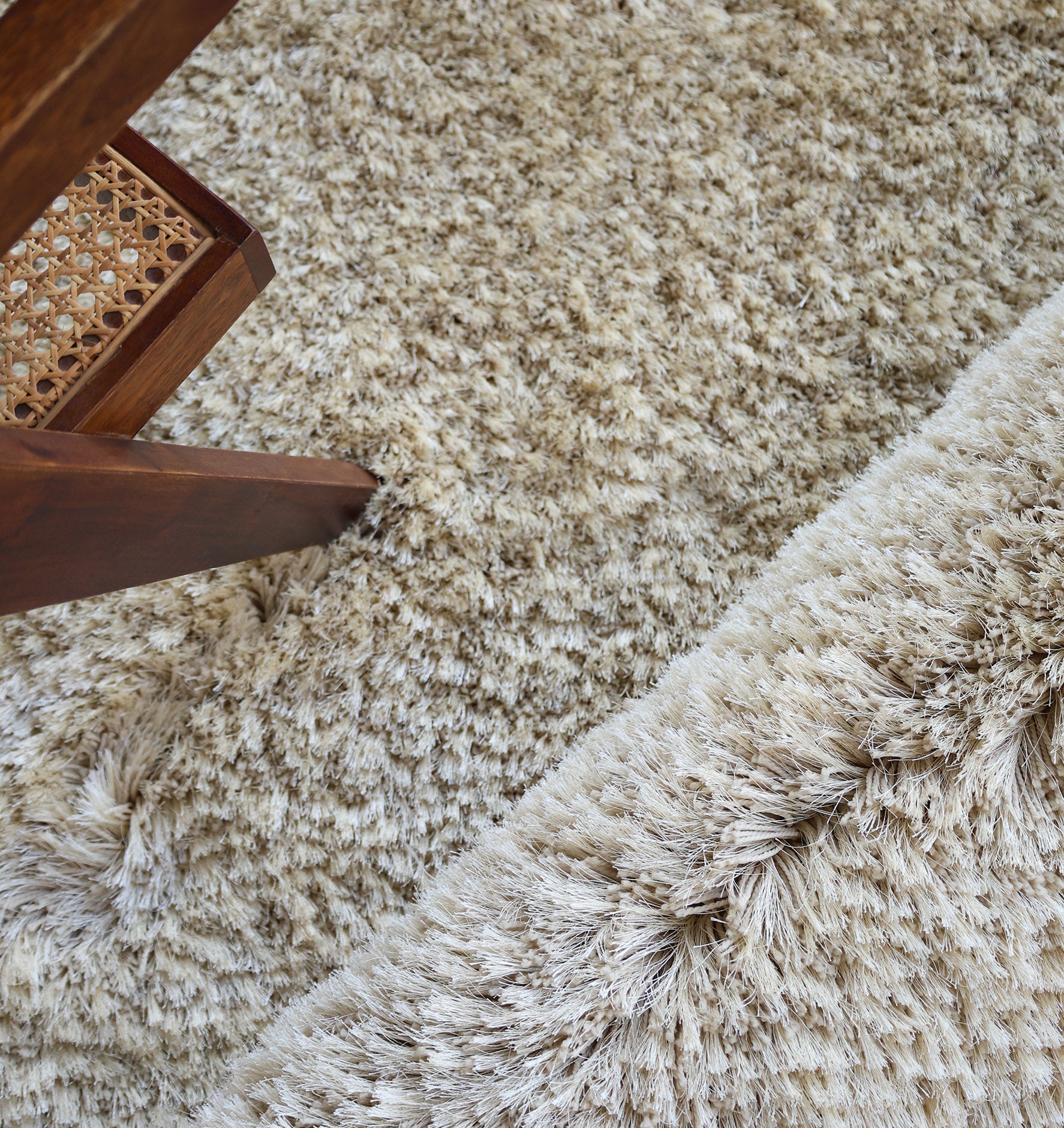 Close-up of the RAMSHA HOME Modern Ultra Soft Shaggy Carpet for Bedroom - SG 041 with long beige fibers, ideal for modern interiors, partially covered by a wooden chair with a woven cane seat on the left.