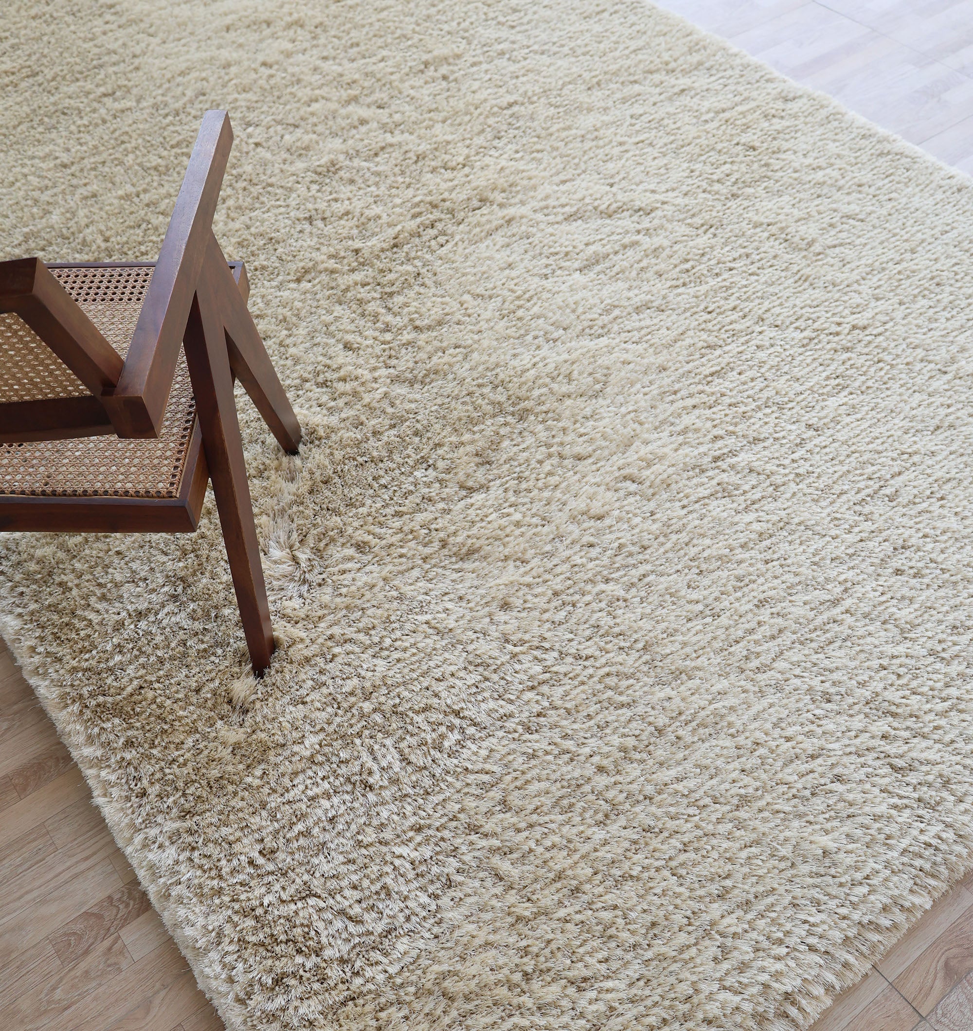 A wooden chair with a woven cane seat sits on the Modern Ultra Soft Shaggy Carpet for Bedroom - SG 041 by RAMSHA HOME, placed atop a wooden floor, adding warmth and comfort to the space.