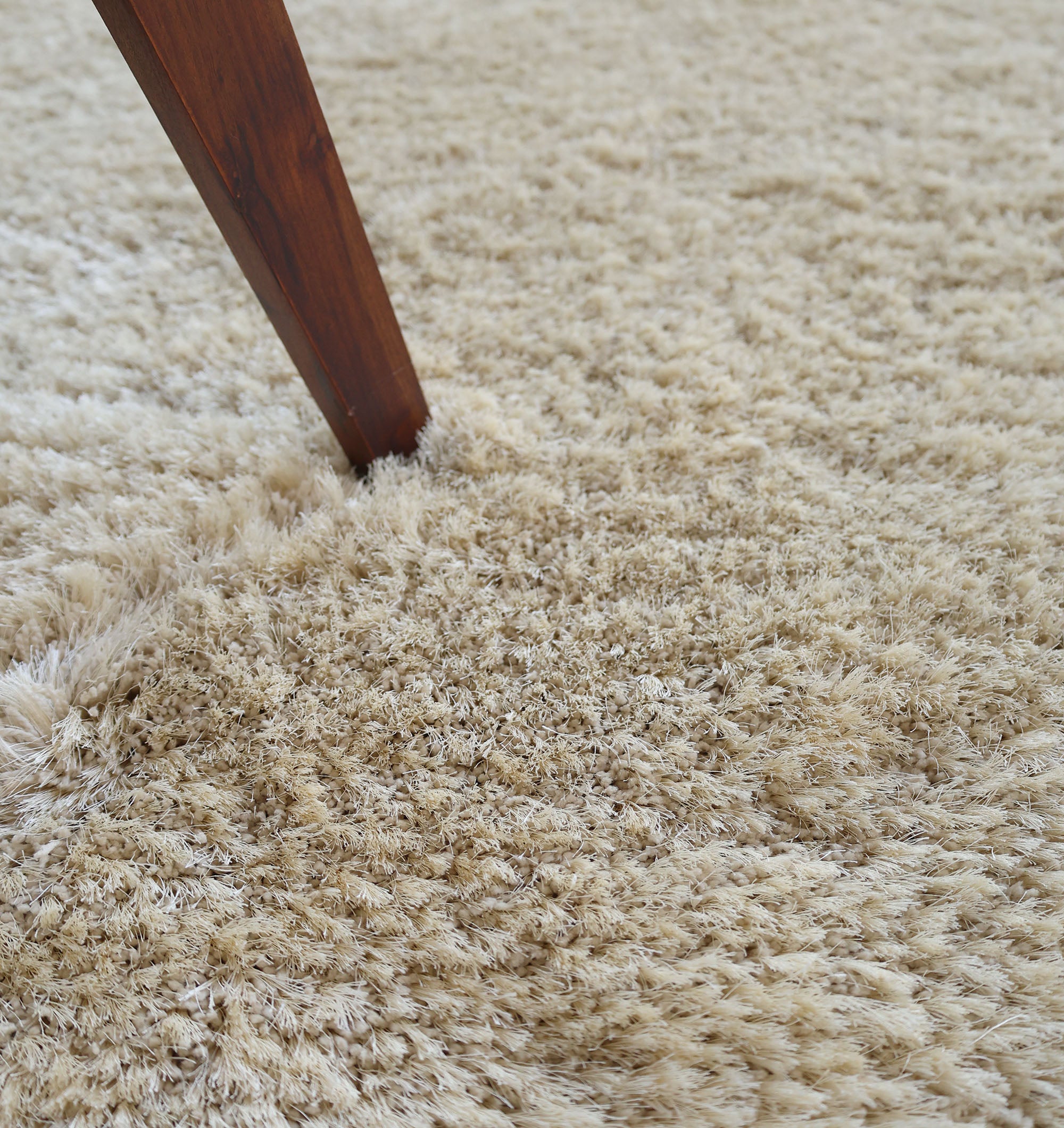 A wooden table leg rests on the RAMSHA HOME Modern Ultra Soft Shaggy Carpet for Bedroom - SG 041, highlighting its plush, cozy texture—a great accent for modern interiors.