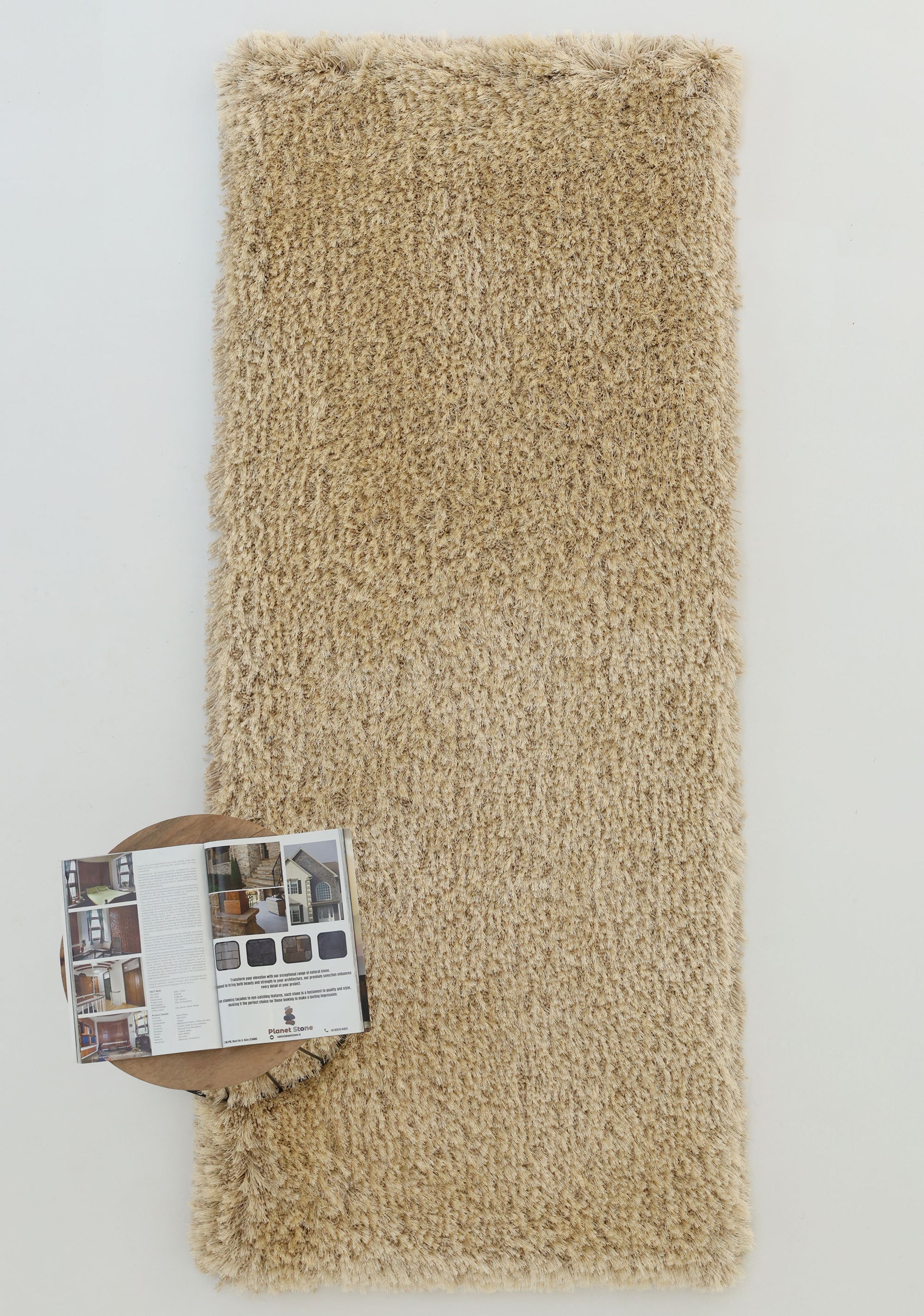 The RAMSHA HOME Modern Ultra Soft Shaggy Carpet for Bedroom - SG 041 lies on a white surface with an open magazine and a round, brown object at one corner, adding cozy style to contemporary interiors.