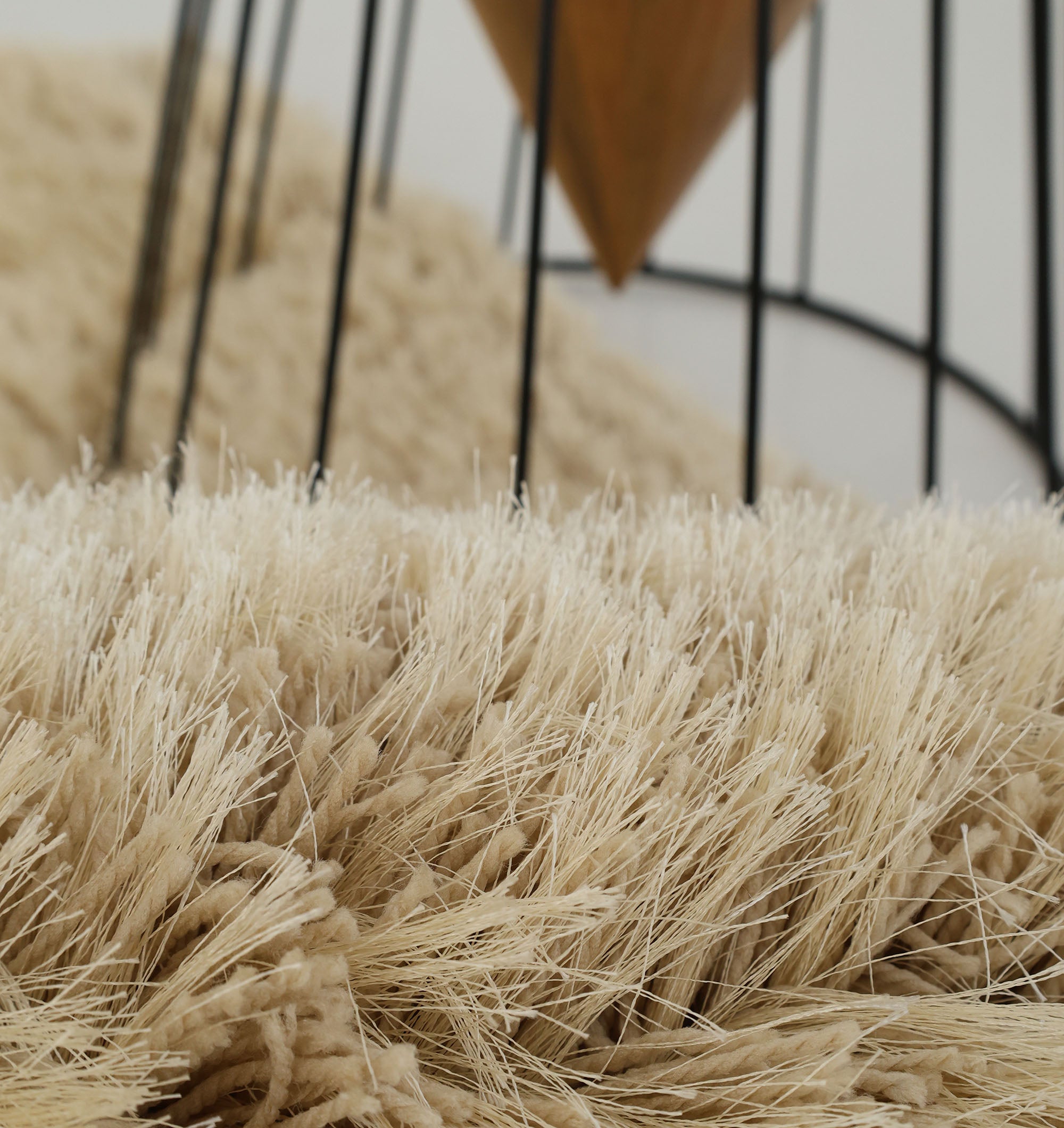 Close-up of the RAMSHA HOME Modern Ultra Soft Shaggy Carpet for Bedroom - SG 041, showing its long, plush beige fibers with a black metal furniture leg and wooden accent—ideal for adding comfort to contemporary spaces.