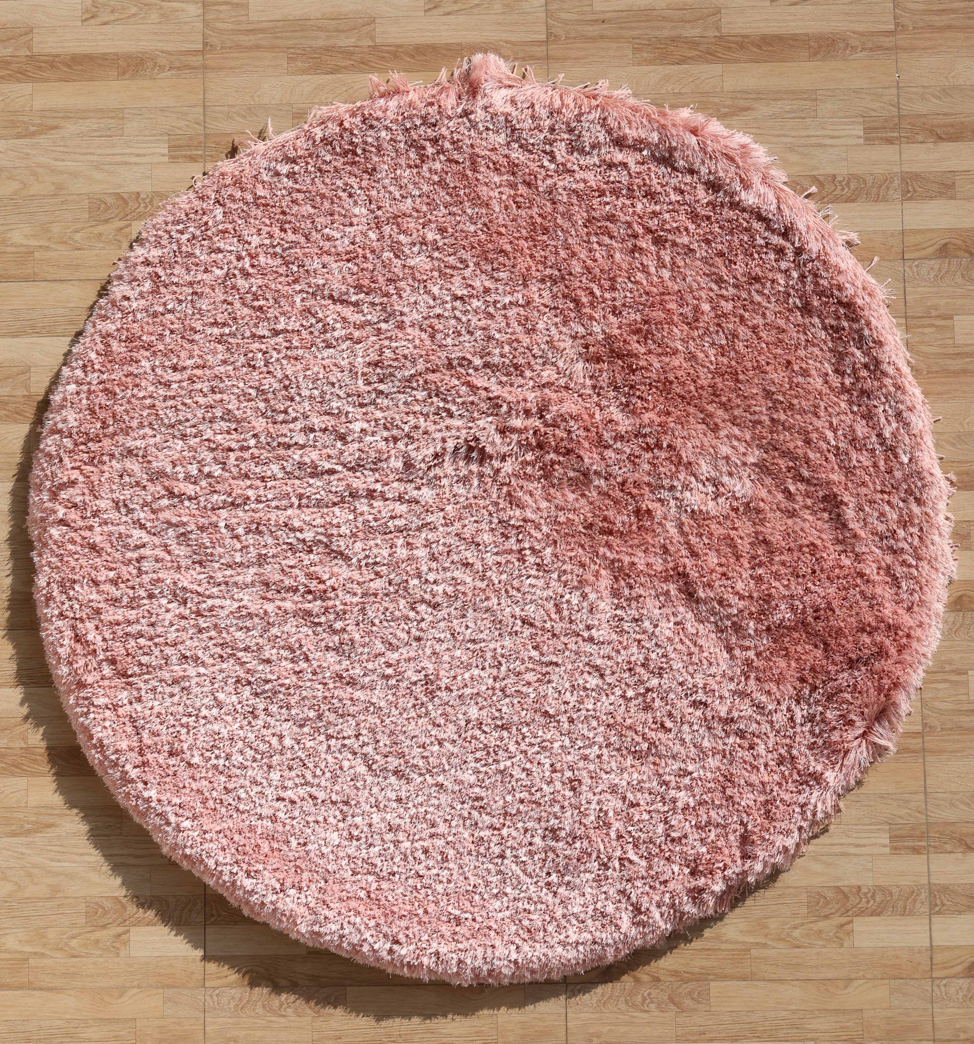 The RAMSHA HOME Modern Ultra Soft Pink Shaggy Carpet for Bedroom (SG 042) features a round design and plush, slightly uneven texture, shown here atop a light wood-patterned floor.