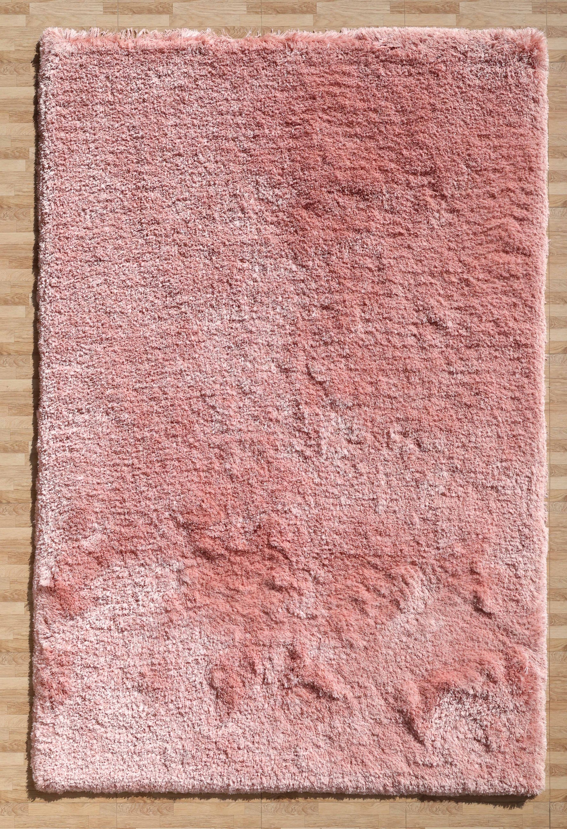 The RAMSHA HOME Modern Ultra Soft Pink Color Shaggy Carpet for Bedroom - SG 042 features a fluffy texture and subtle shade variations, adding cozy, uneven charm to your space as it rests on a light brown wooden floor.