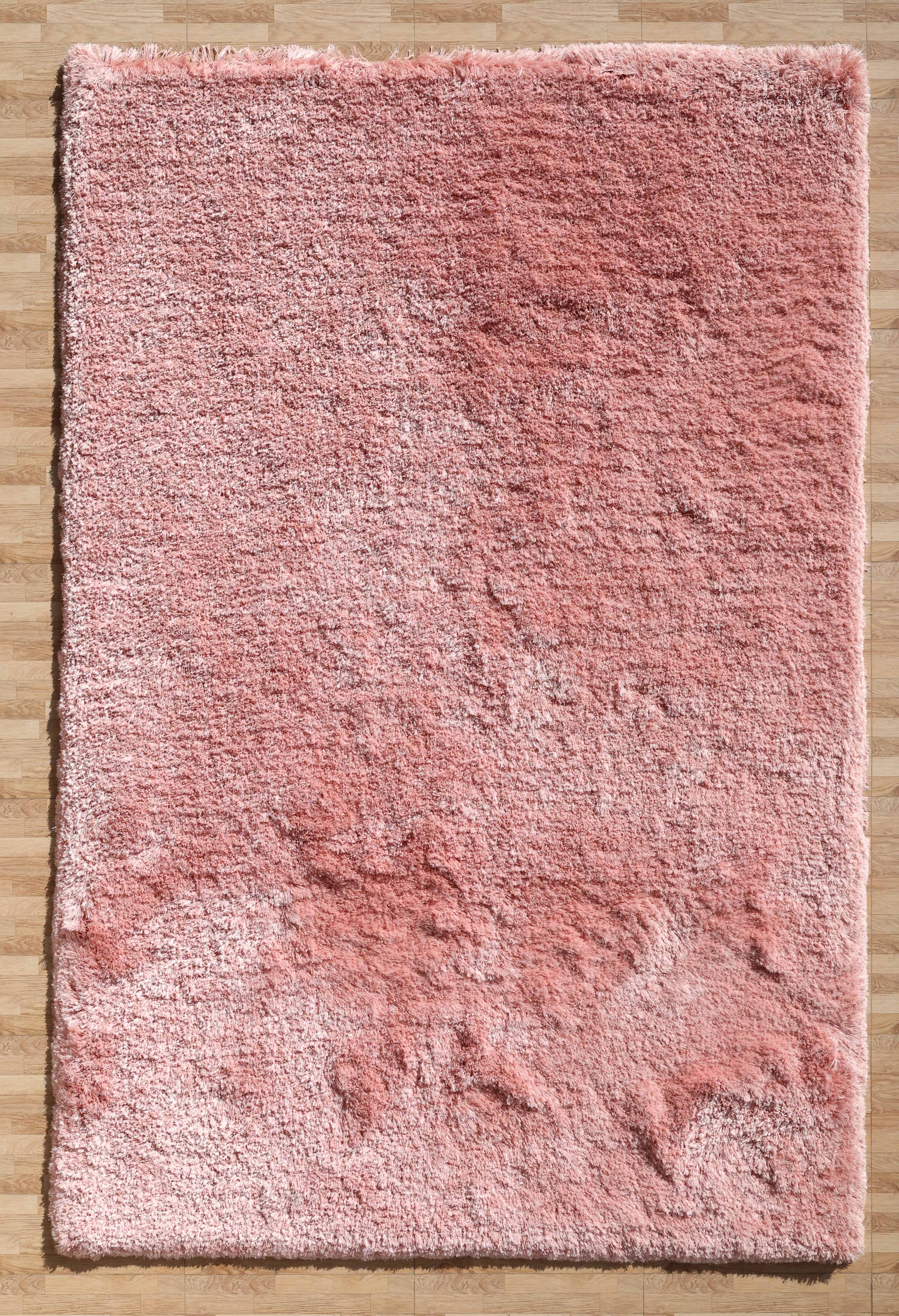 The RAMSHA HOME Modern Ultra Soft Pink Color Shaggy Carpet for Bedroom - SG 042 features a fluffy texture and subtle shade variations, adding cozy, uneven charm to your space as it rests on a light brown wooden floor.