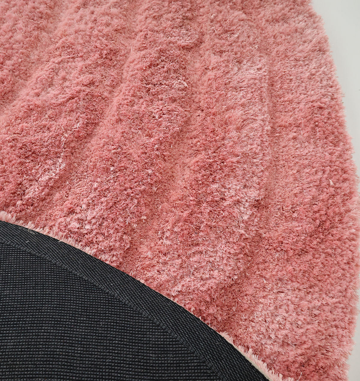 Close-up of the RAMSHA HOME Gold irregular Shaped Home Decor Shaggy Rug - SG 042 3D, featuring a unique curved edge and pink shaggy surface, partially showing its black non-slip backing on a white background.