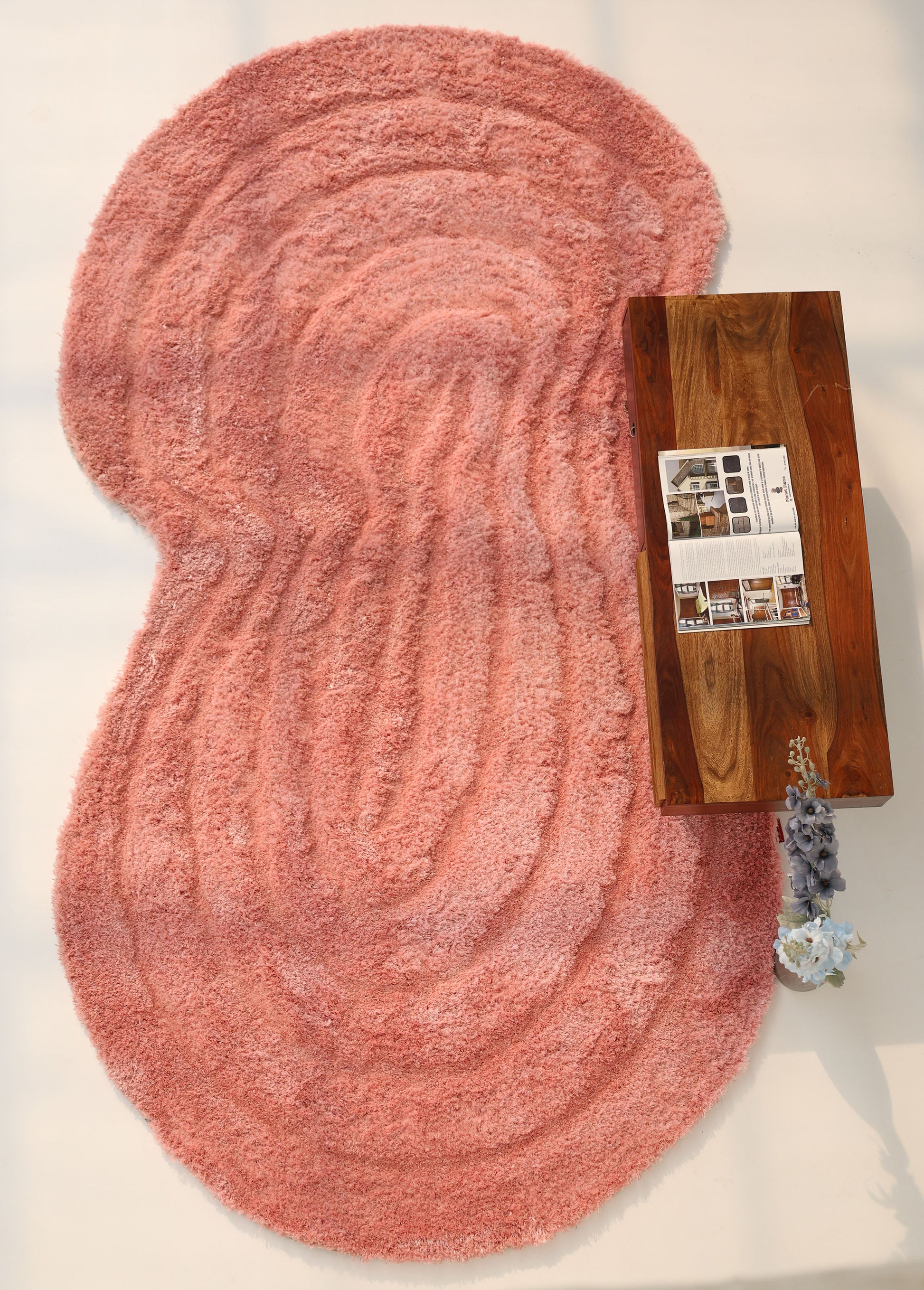 The RAMSHA HOME Gold irregular Shaped Home Decor Shaggy Rug - SG 042 3D with wavy patterns sits next to a wooden coffee table holding an open magazine and a small vase of flowers.
