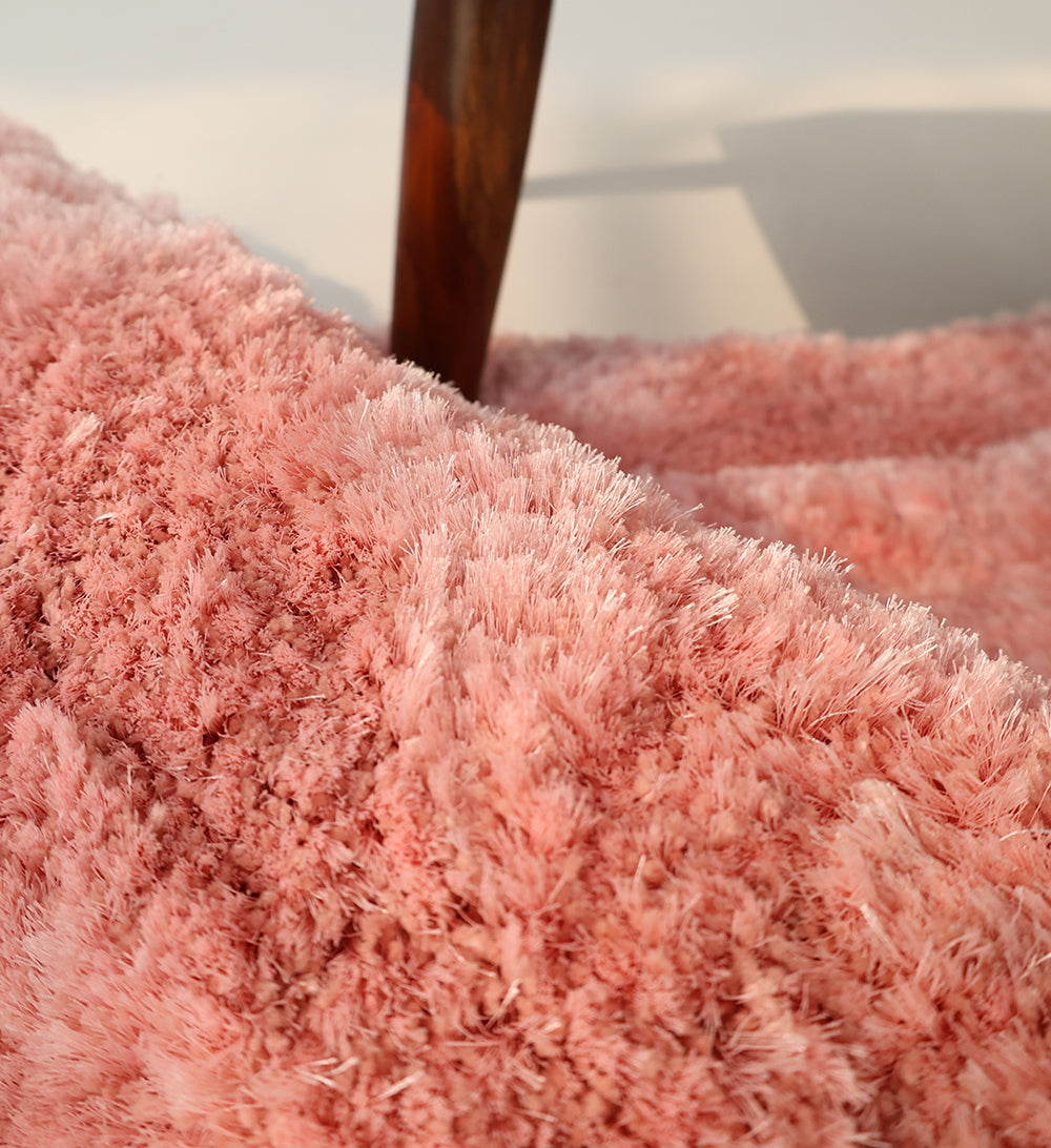 Close-up of the RAMSHA HOME Modern Ultra Soft Pink Color Shaggy Carpet for Bedroom (SG 042), showing its plush, fluffy texture and cozy charm with a wooden furniture leg in the background—ideal for contemporary interiors.