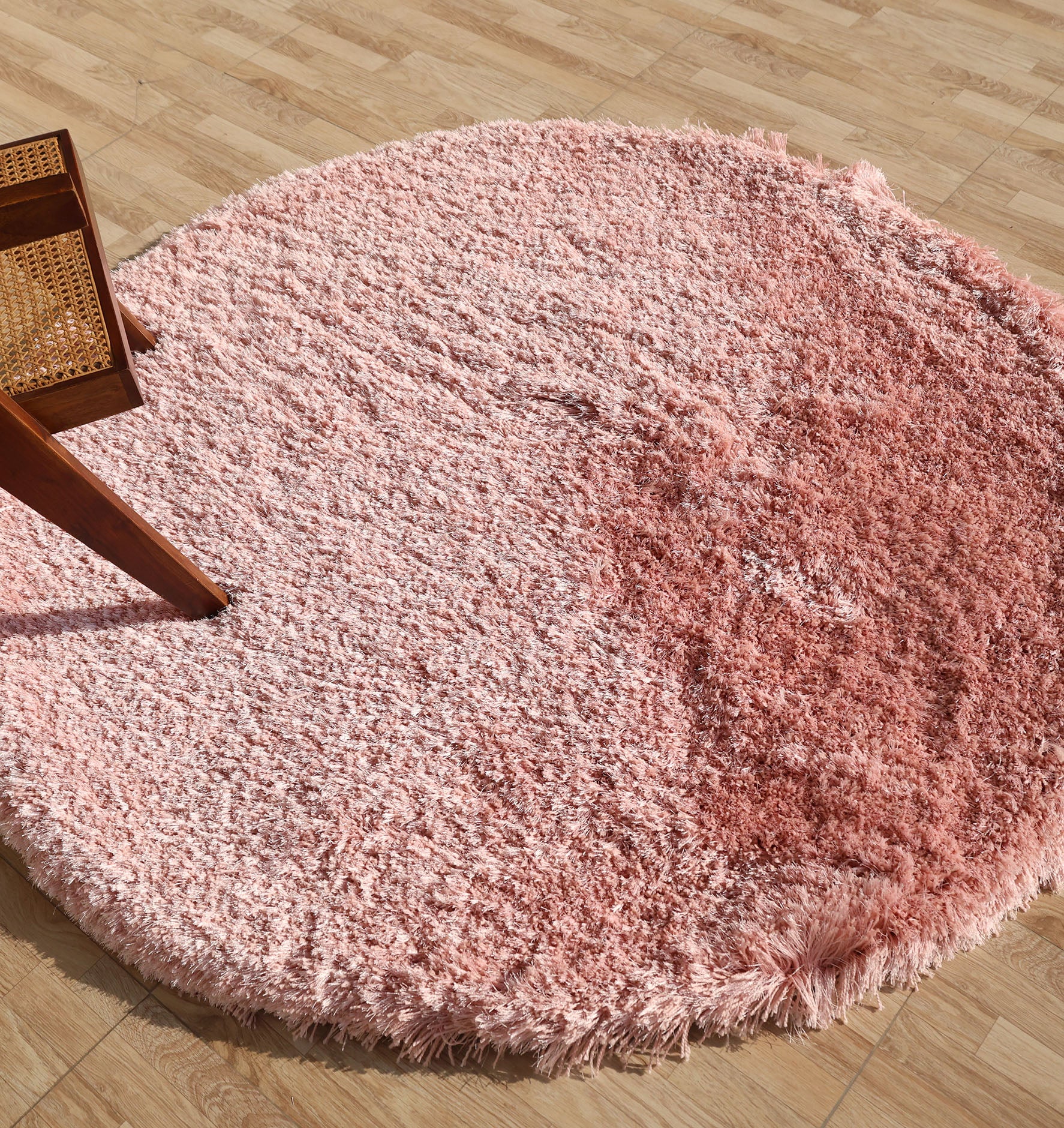 The RAMSHA HOME Modern Ultra Soft Pink Color Shaggy Carpet for Bedroom - SG 042, featuring a plush gradient design, is displayed on a light wood floor with part of a wooden chair with woven seat visible at the rug’s edge.