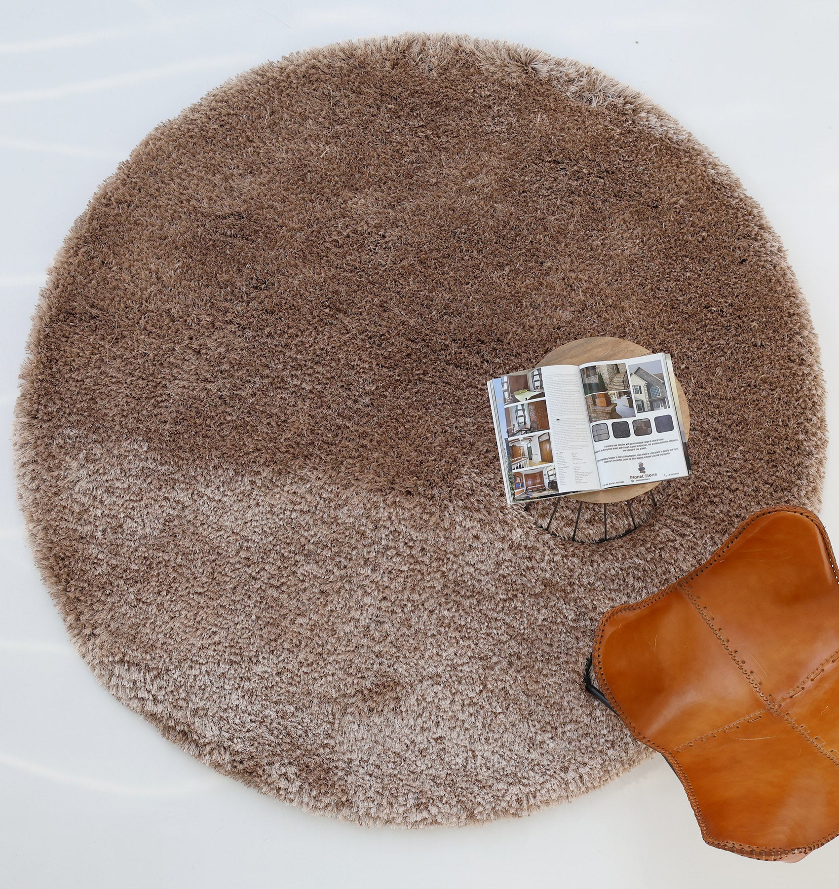 The RAMSHA HOME Soft Plush Brown Shaggy Rug (SG 043) sits on a light floor, with a small table holding an open magazine and a brown leather chair nearby.