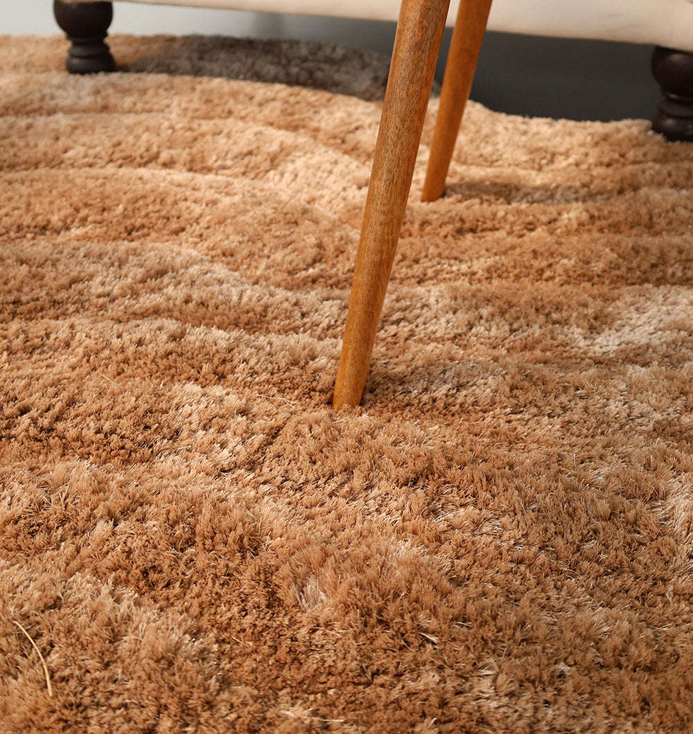 A close-up of the RAMSHA HOME Luxury Soft Touch Irregular Shaggy Area Rug - SG 043 3D shows wooden furniture legs pressing into its plush, light brown fibers, creating visible indentations.