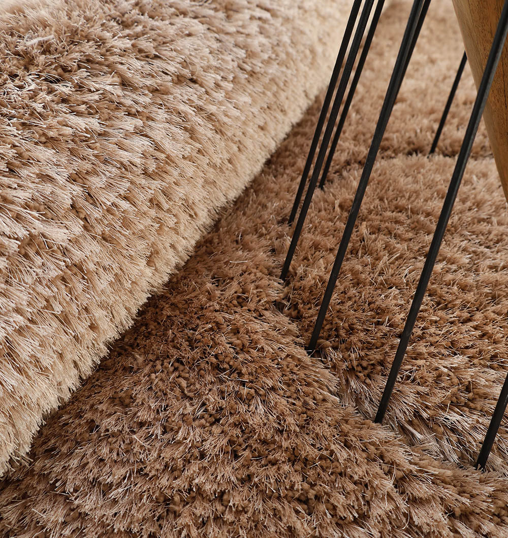 Close-up of the RAMSHA HOME Soft Plush Brown Shaggy Rug for Living Room - SG 043, partially rolled near black metal furniture legs, showcasing its thick plush fibers and inviting texture.