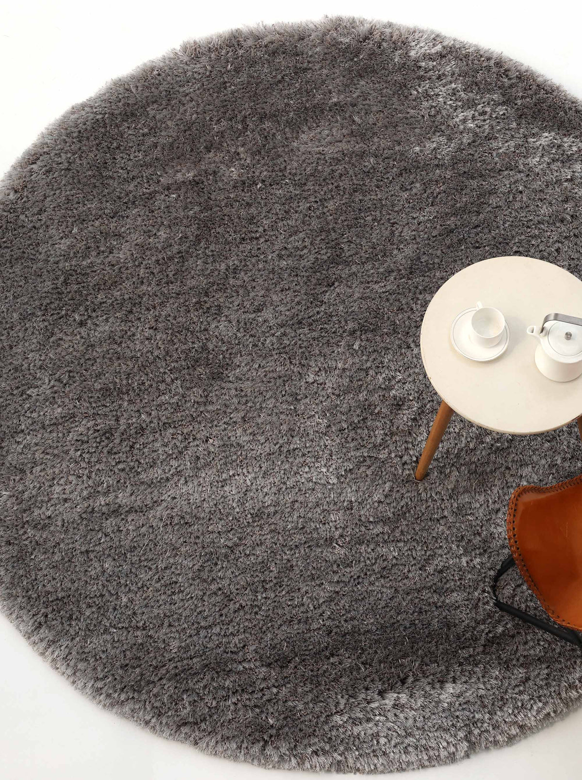 The RAMSHA HOME Soft Plush Grey Shaggy Rug for Living Room - SG 044 sits beneath a small round side table holding a white tea set, with a brown chair partially visible on the right.