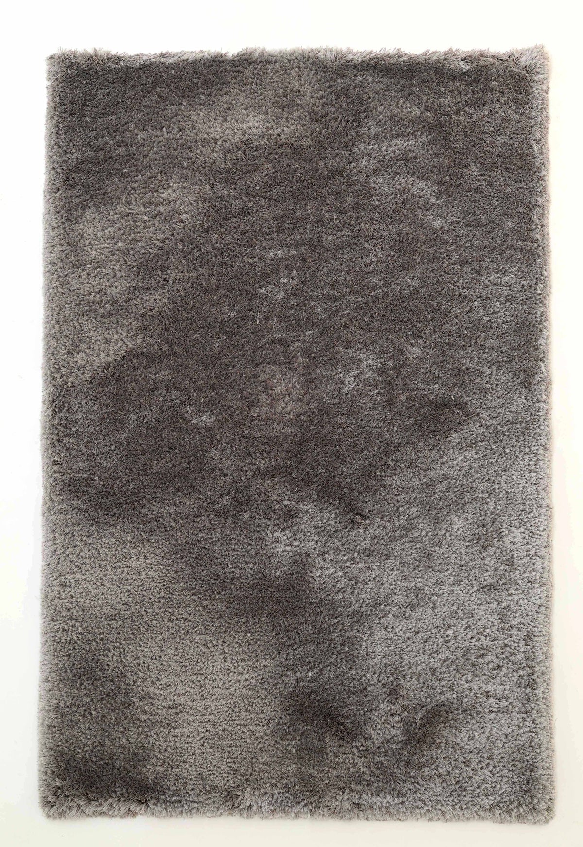 A rectangular RAMSHA HOME Soft Plush Grey Shaggy Rug for Living Room (SG 044) featuring a soft, textured surface with uneven, darker gray patches, displayed on a white background.