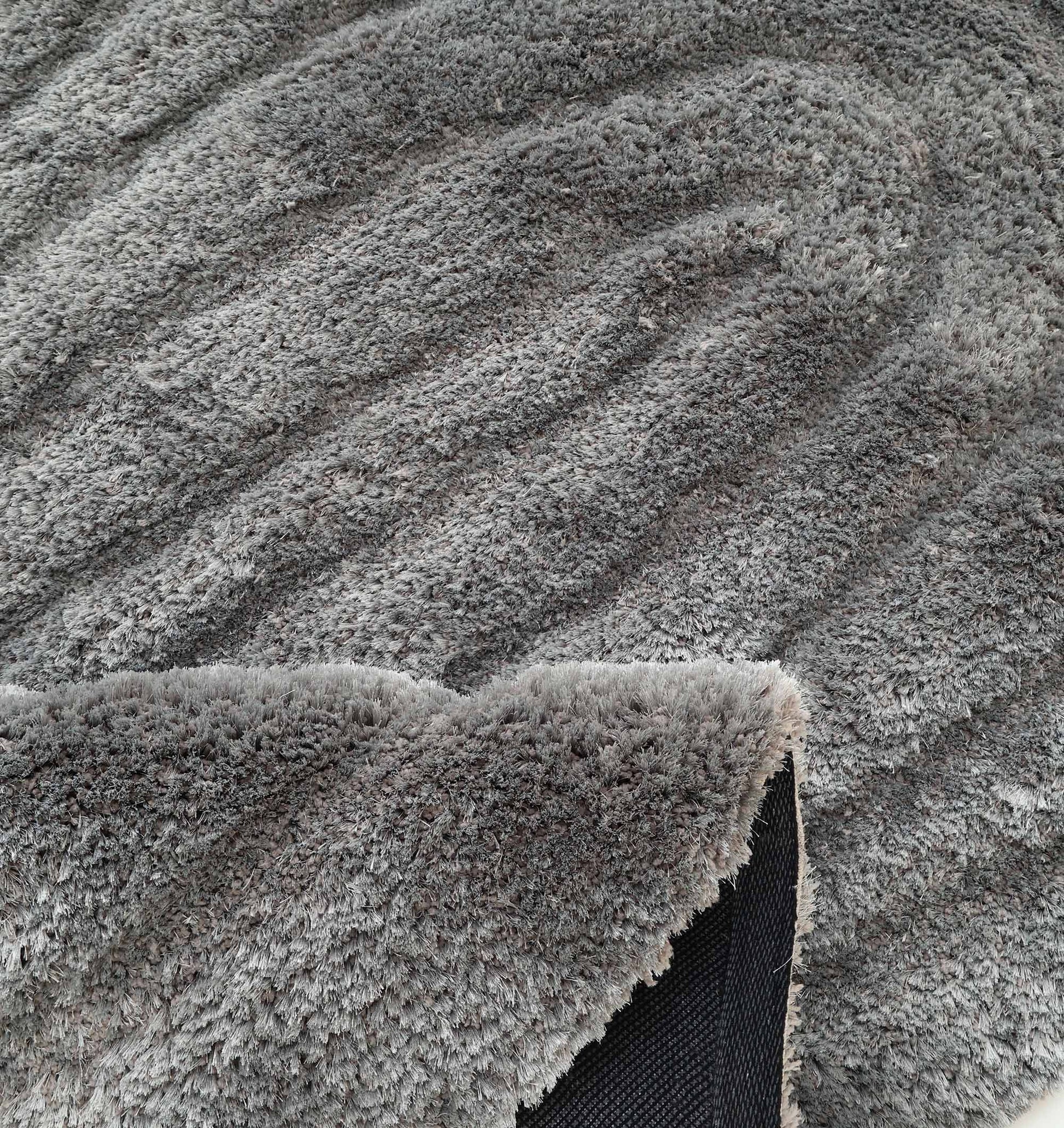 The RAMSHA HOME Luxury Soft Grey Irregular Shaggy Area Rug - SG 044 3D features wavy patterns and a flipped corner showing its black, non-slip backing; perfect for adding modern texture and style to any space.