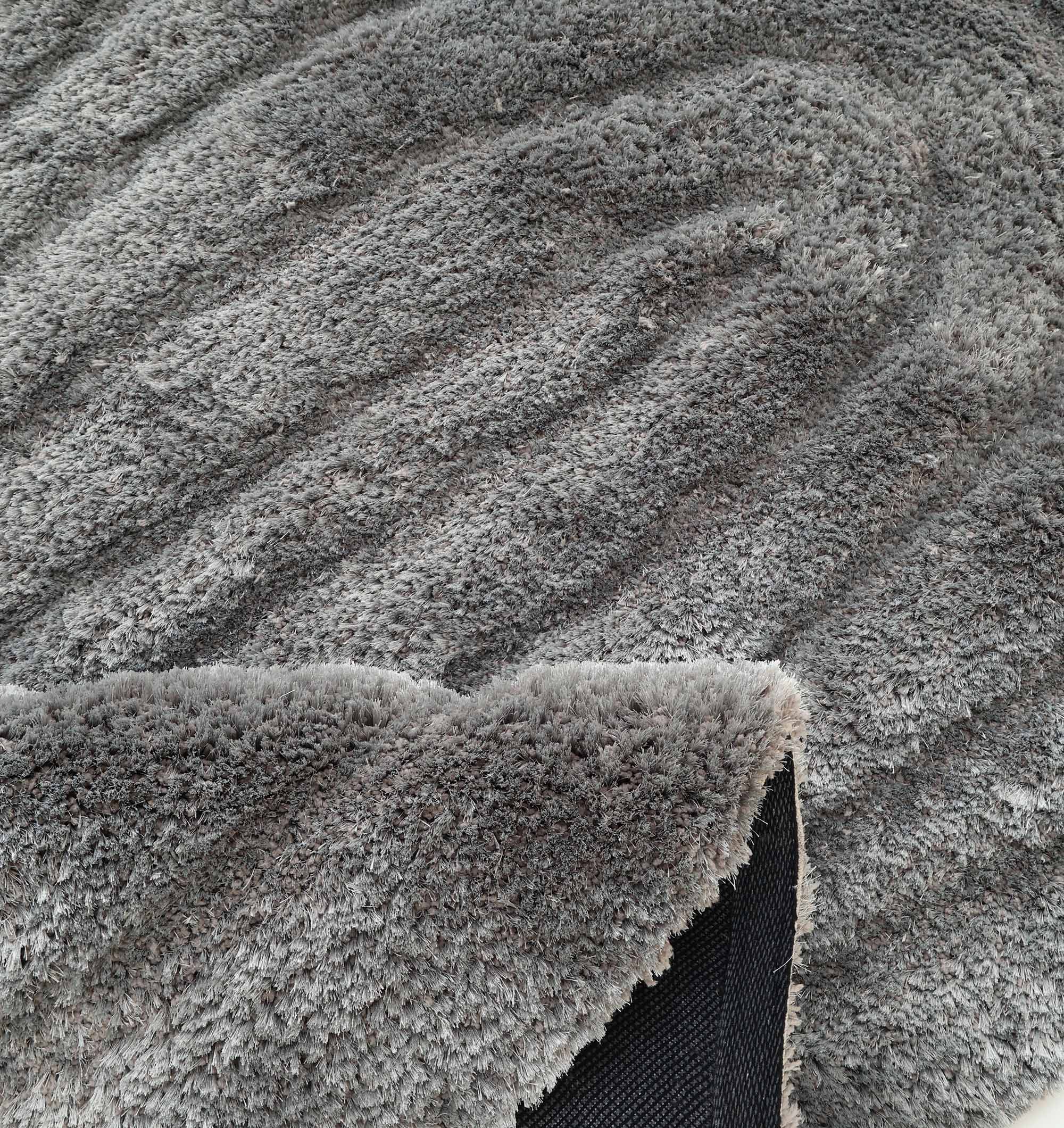 The RAMSHA HOME Luxury Soft Grey Irregular Shaggy Area Rug - SG 044 3D features wavy patterns and a flipped corner showing its black, non-slip backing; perfect for adding modern texture and style to any space.