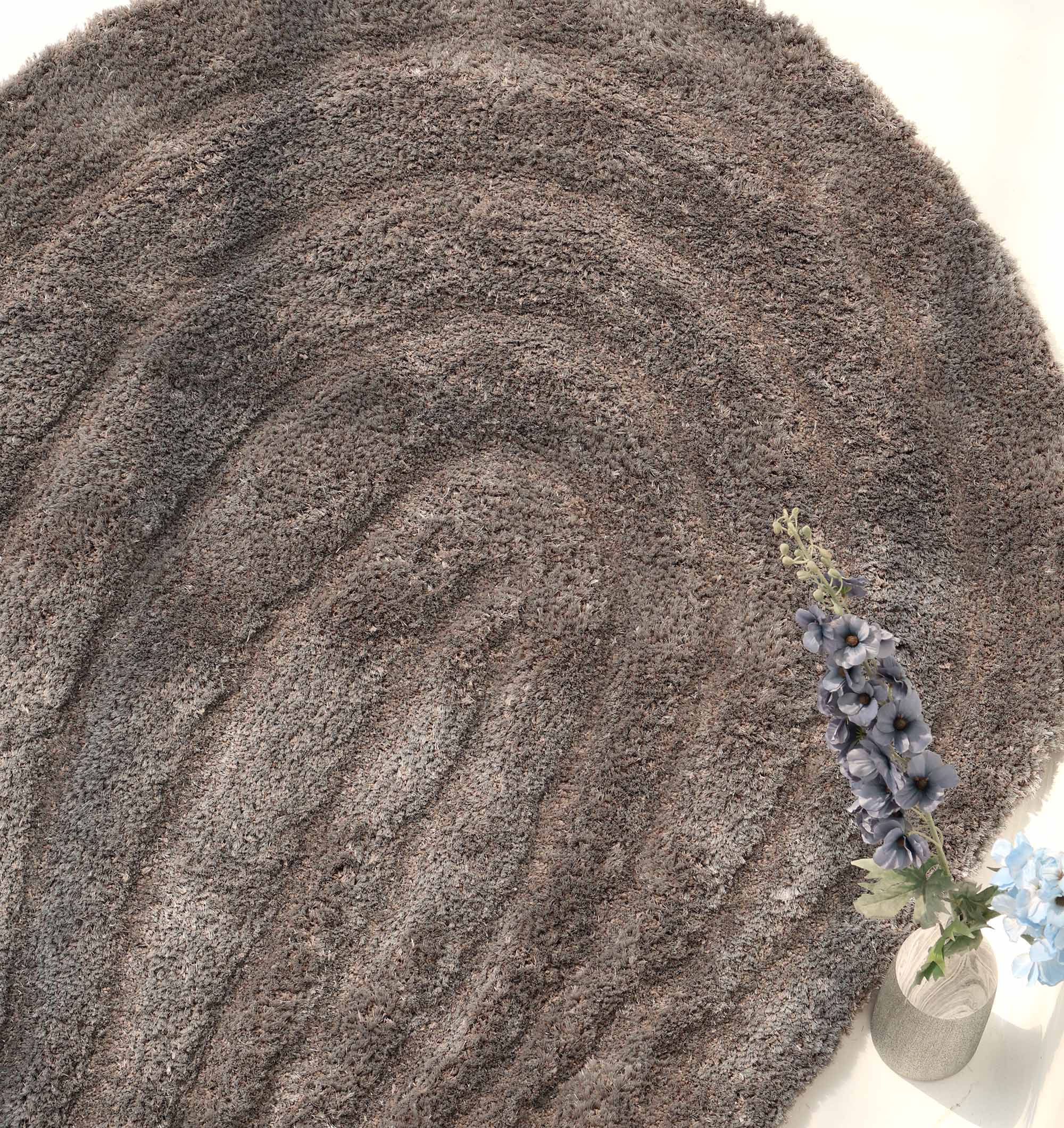 The RAMSHA HOME Luxury Soft Grey Irregular Shaggy Area Rug - SG 044 3D adds plush texture, while a clear vase of tall purple and blue flowers at its edge pops against the neutral floor for a sleek, modern touch.