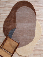The RAMSHA HOME Contemporary Freeform Plush Rug - SG 047, featuring overlapping brown, beige, tan, and gray shapes, lies on a light wood floor with a wooden chair and woven cane seat in the lower left corner.