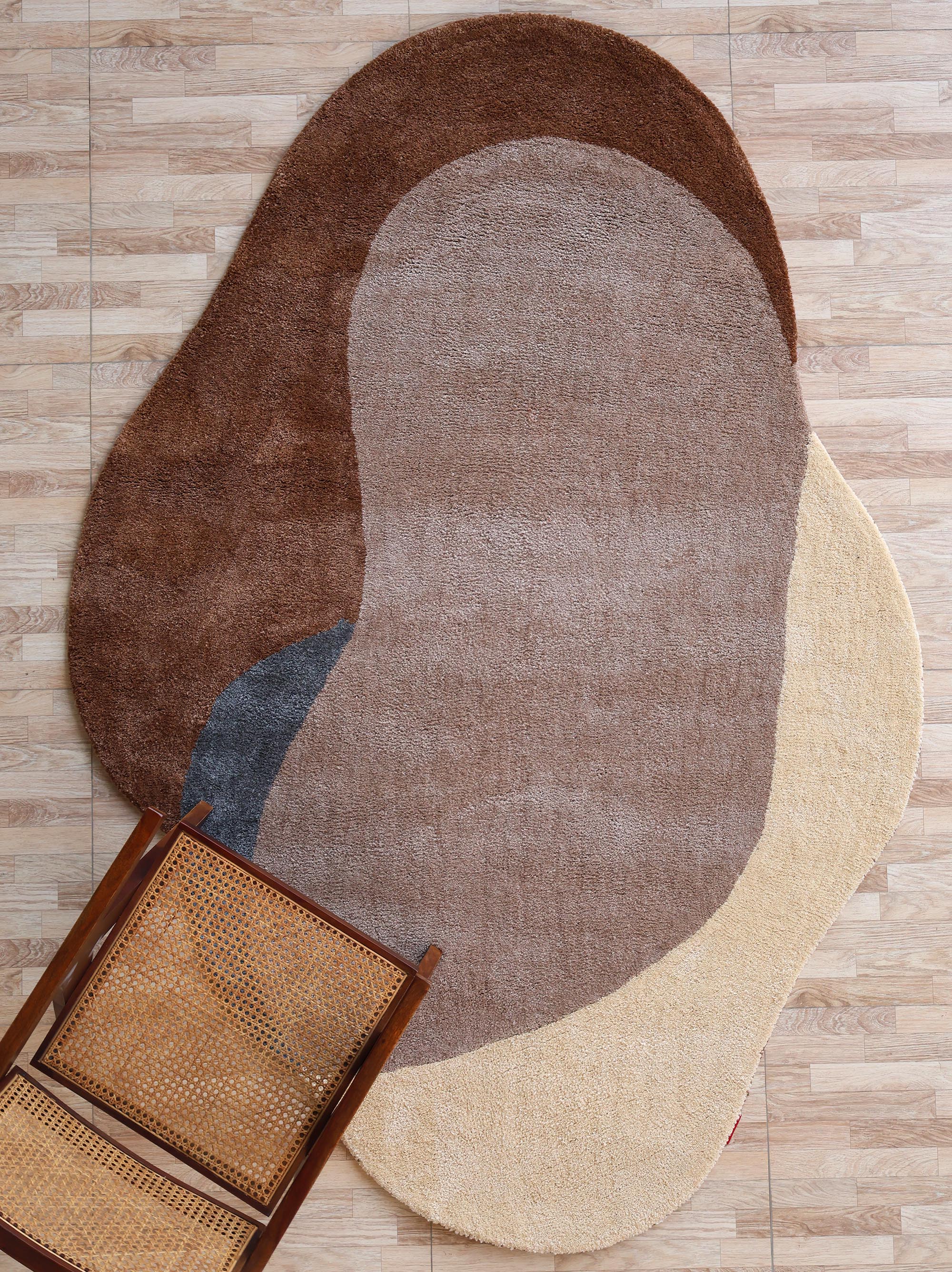 The RAMSHA HOME Contemporary Freeform Plush Rug - SG 047, featuring overlapping brown, beige, tan, and gray shapes, lies on a light wood floor with a wooden chair and woven cane seat in the lower left corner.