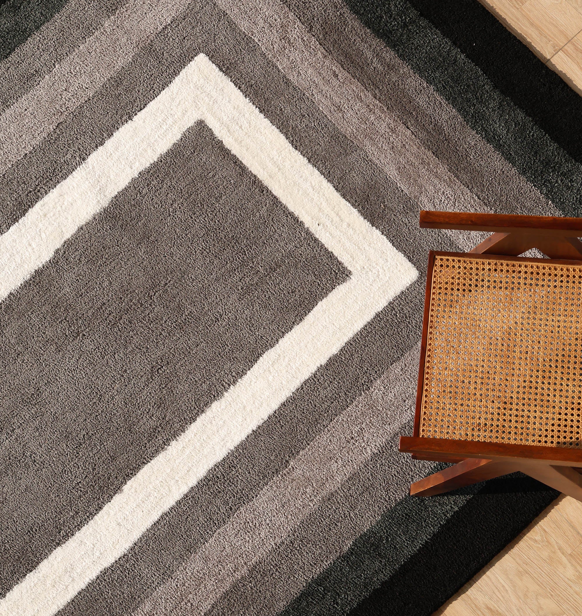 A wooden chair with a woven cane seat sits in the corner atop the RAMSHA HOME Black Shaggy Area Rug for Large Living Room - SG 049, which features plush geometric patterns in gray, black, and white bands on a wooden floor.