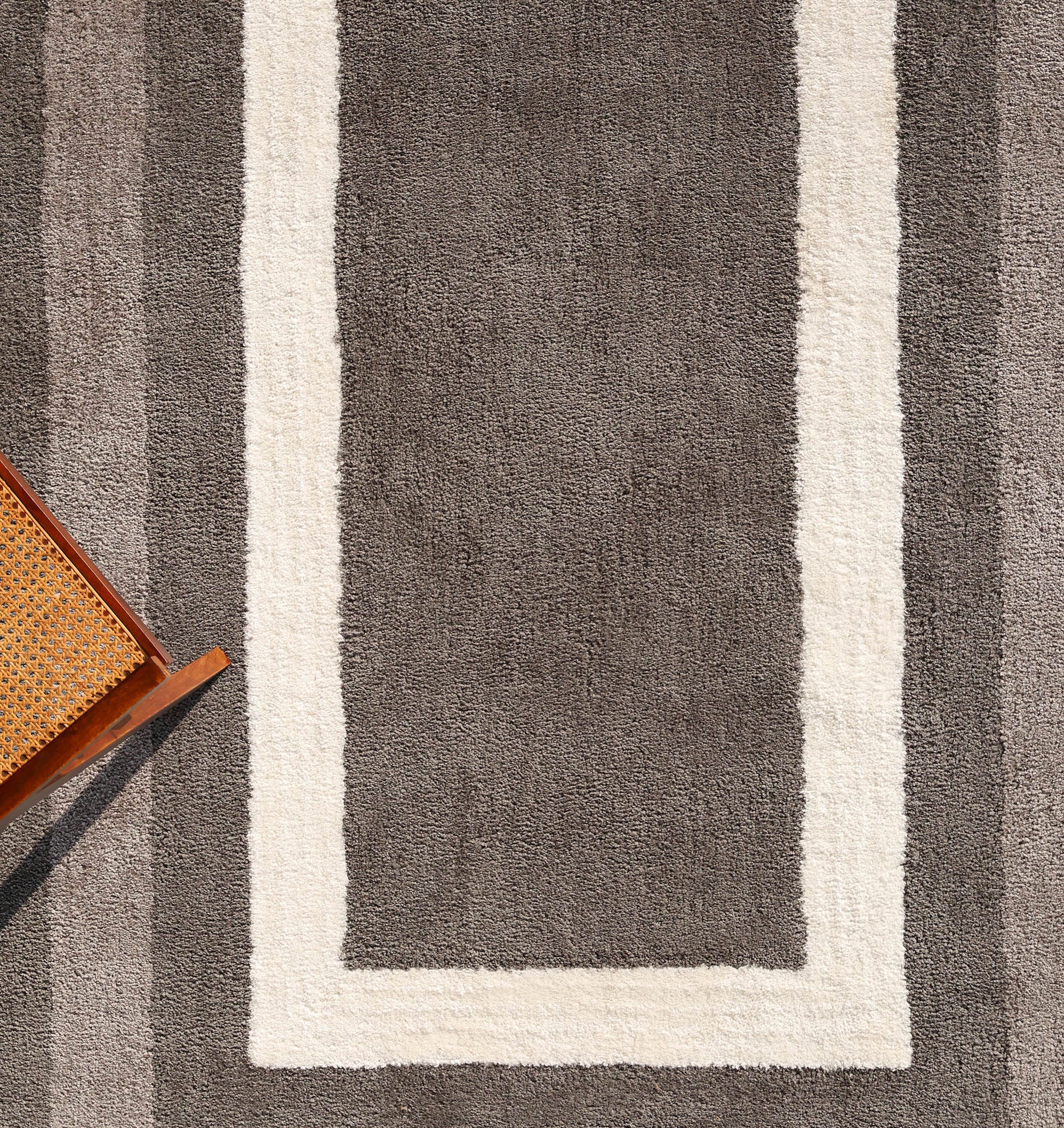 The RAMSHA HOME Black Shaggy Area Rug for Large Living Room - SG 049 features a textured shag with a wide white rectangular border, shown from above. A wooden chair with a woven seat is visible in the bottom left corner.