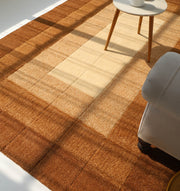 A sunlit living room showcases the RAMSHA HOME Modern Beige & Brown circular Shaggy Rug (SG 052), with part of a round side table and an upholstered armchair visible on the right.