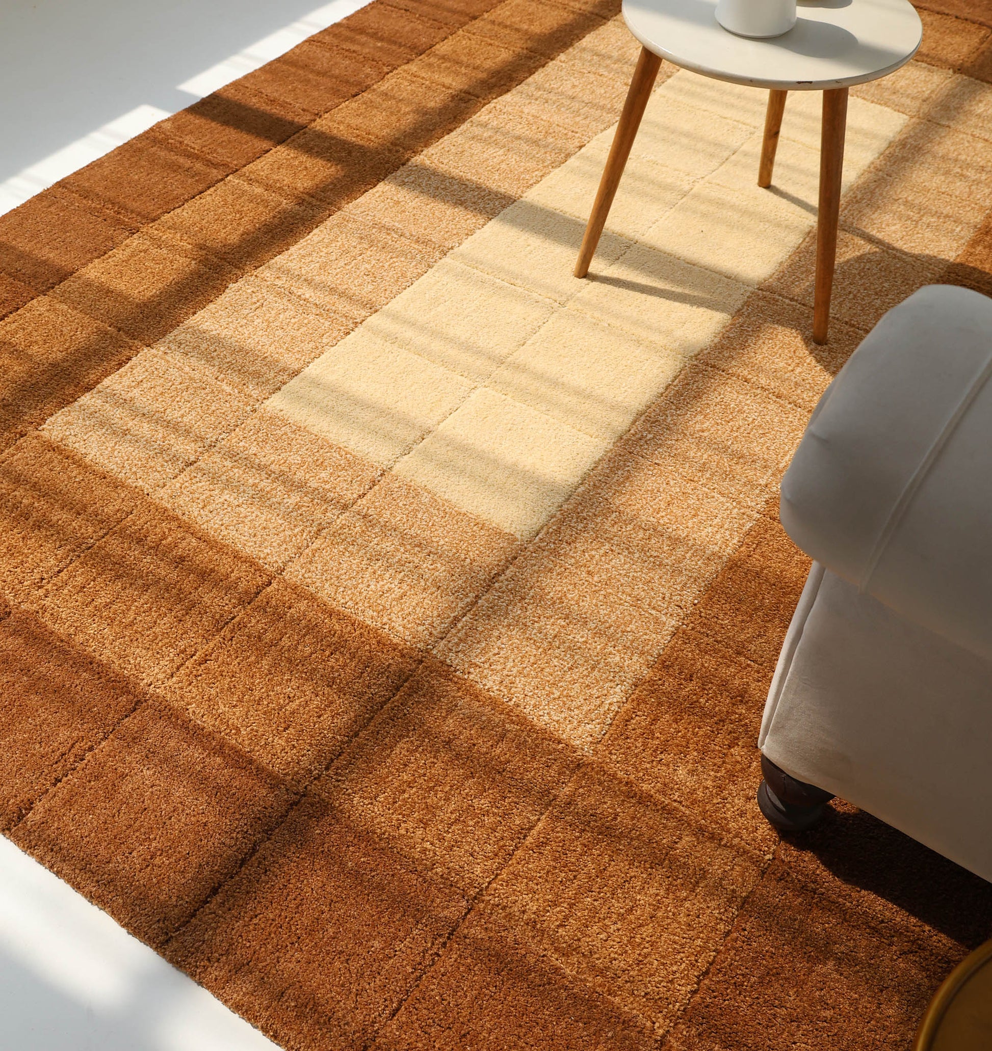 A sunlit living room showcases the RAMSHA HOME Modern Beige & Brown circular Shaggy Rug (SG 052), with part of a round side table and an upholstered armchair visible on the right.