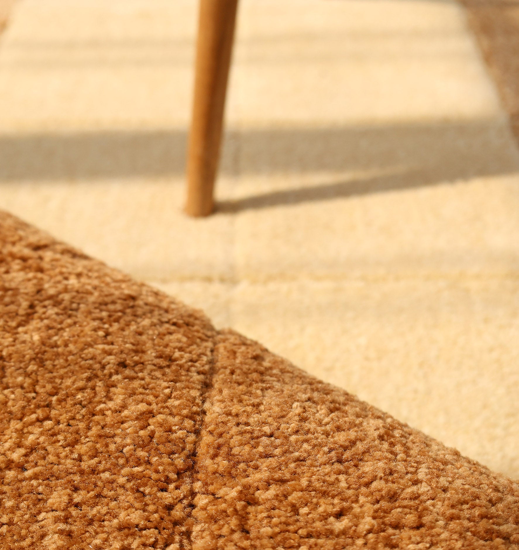 Close-up of the Modern Beige & Brown Circular Shaggy Rug for Living Room - SG 052 by RAMSHA HOME, its soft brown texture and sunlight create warmth, while a wooden furniture leg highlights its contemporary style.