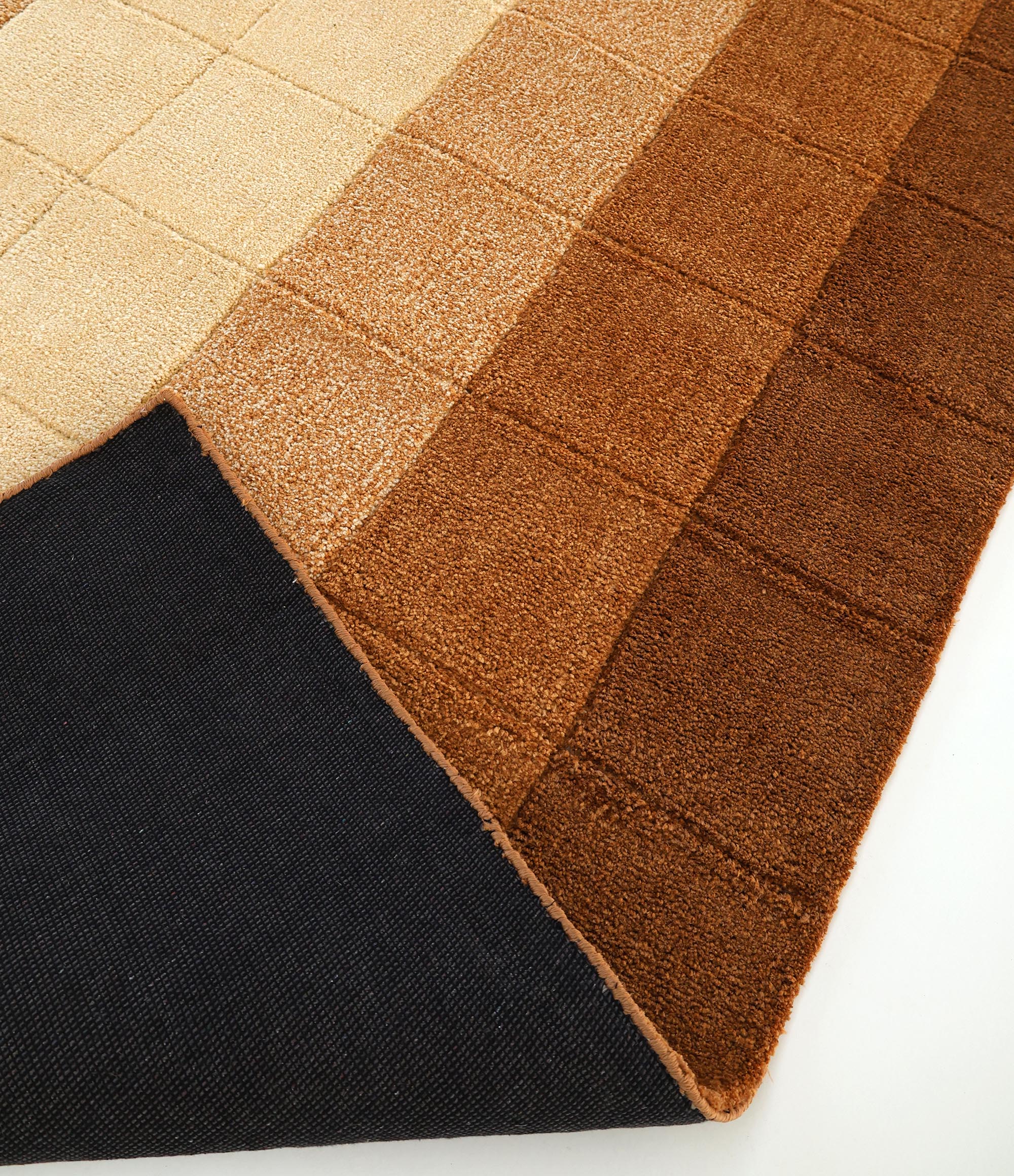 A close-up of the RAMSHA HOME Modern Beige & Brown Circular Shaggy Rug for Living Room - SG 052, featuring a geometric pattern in beige and brown shades, with one corner folded to show its dark textured underside.