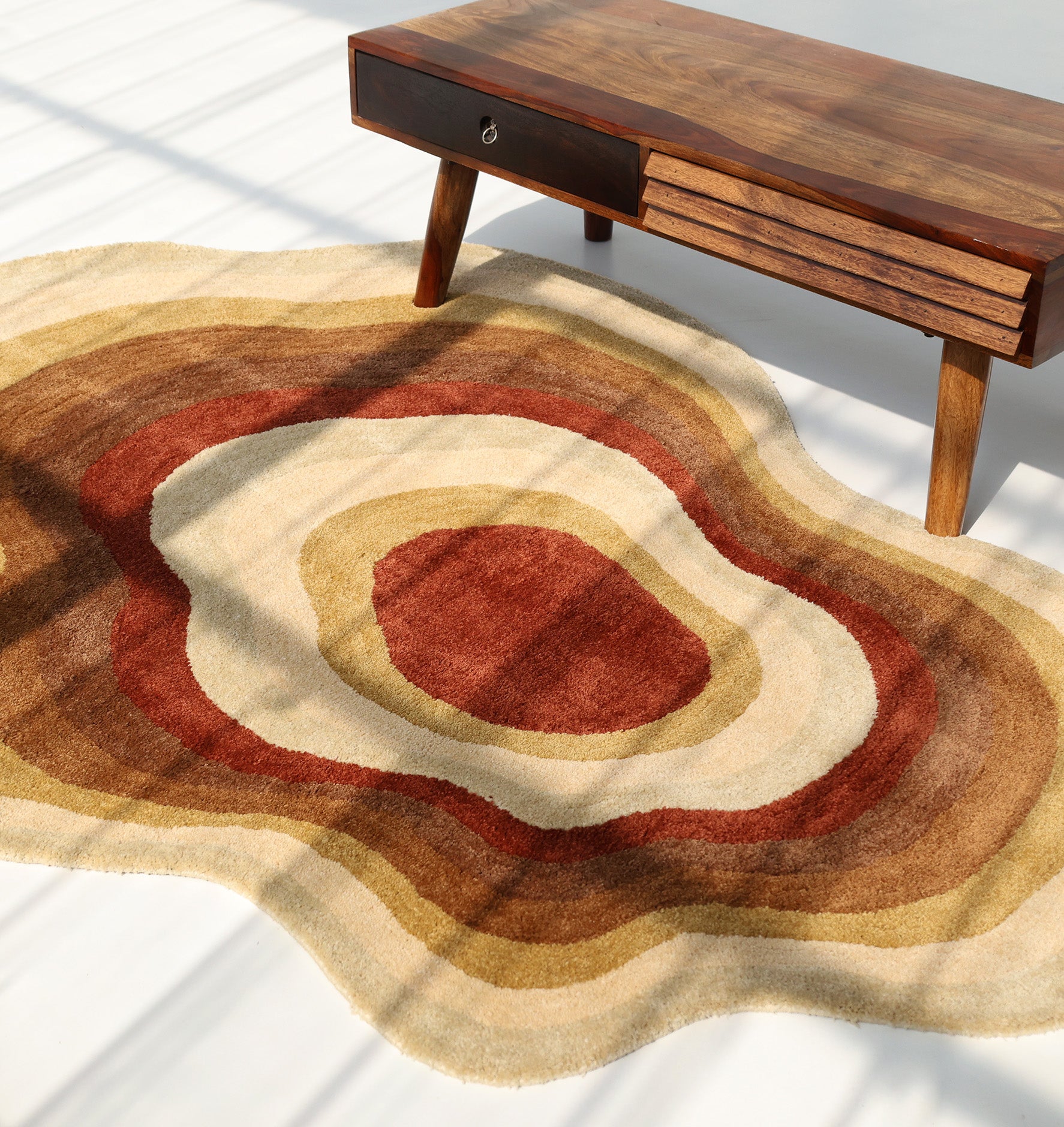 The RAMSHA HOME Modern Layered Border Irregular Soft Shaggy Carpet - SG 055 features retro concentric rings in brown, tan, beige, and rust—ideal for adding cozy décor flair next to a mid-century modern coffee table.