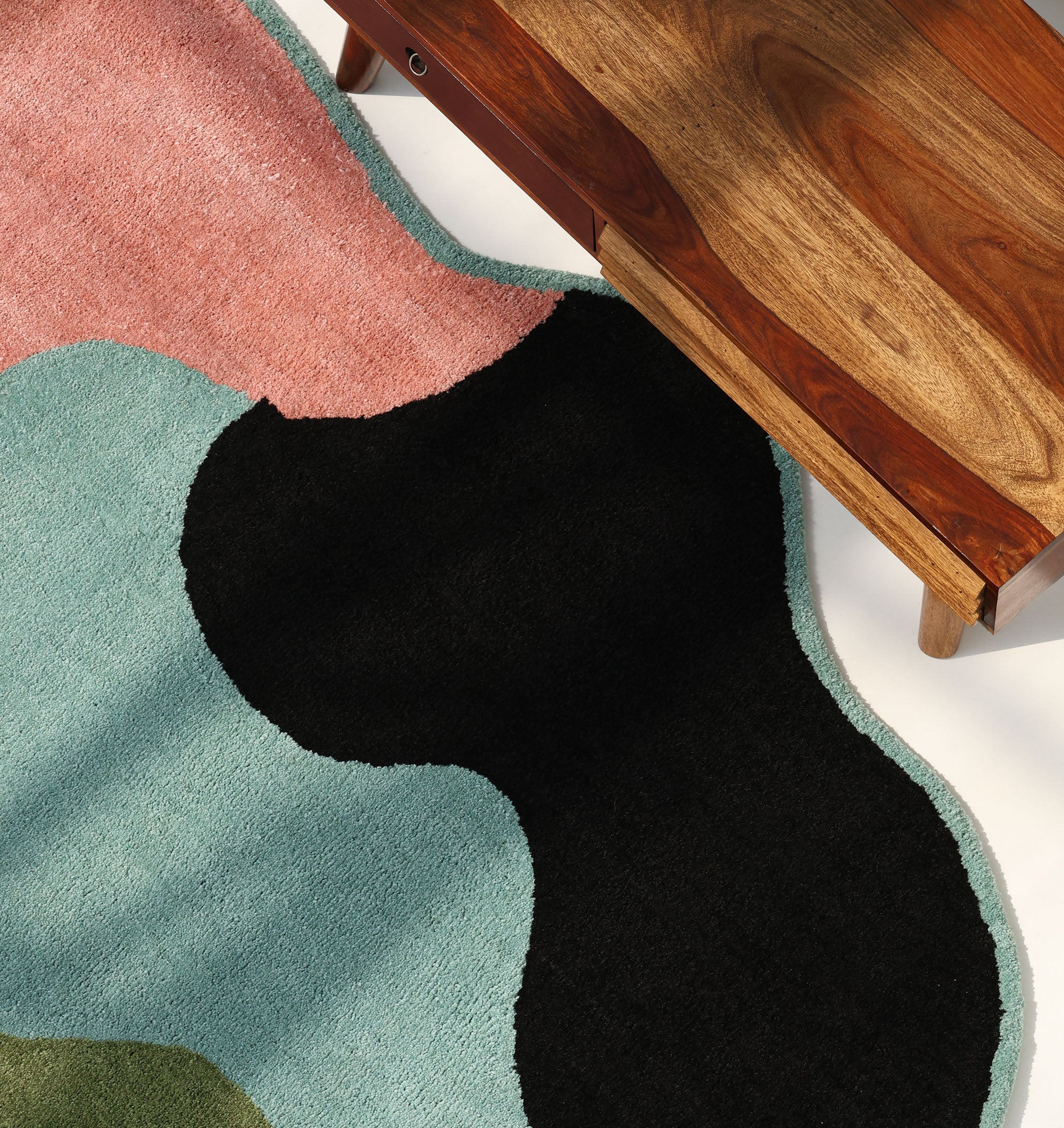 The RAMSHA HOME Modern Multicolor Irregular Soft Shaggy Carpet - SG 056, with vibrant wavy designs, sits beside a richly grained wooden table in natural light—an ideal cozy décor touch.