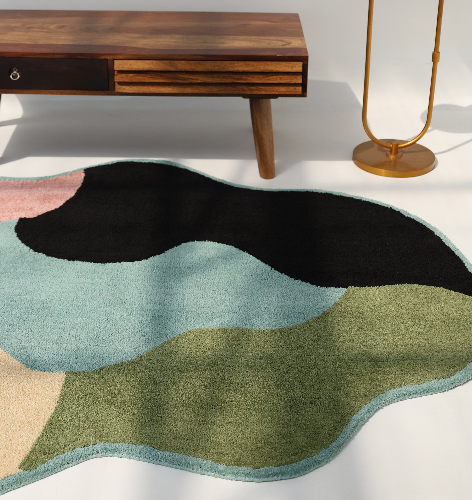 A modern living space with a wooden table, gold floor lamp, and the RAMSHA HOME Modern multicolor Irregular Soft Shaggy Carpet - SG 056 featuring abstract color blocks in black, green, blue, beige, and pink.