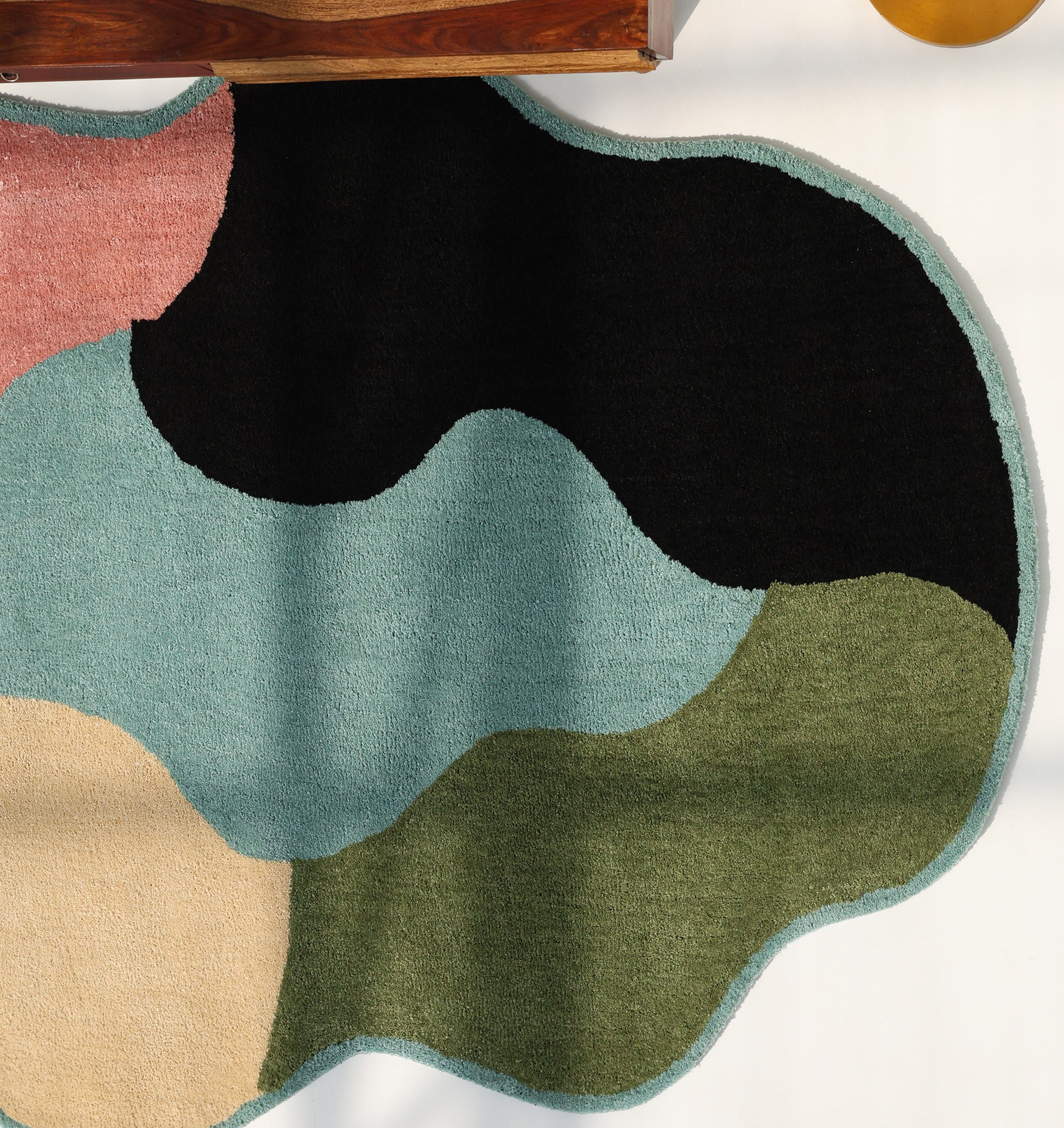 The RAMSHA HOME Modern multicolor Irregular Soft Shaggy Carpet - SG 056, with abstract shapes in black, teal, green, peach, and pink, adds a stylish touch on a light floor next to partially visible wooden furniture.