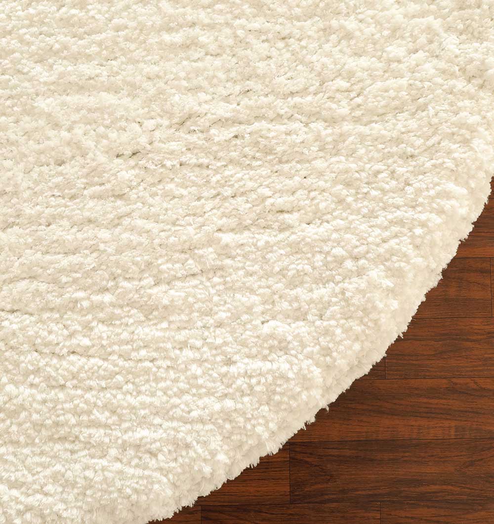 A close-up of the RAMSHA HOME Round Soft White Shaggy Rug - SG 06, featuring a plush texture and round shape, partially covering a dark brown wooden floor.