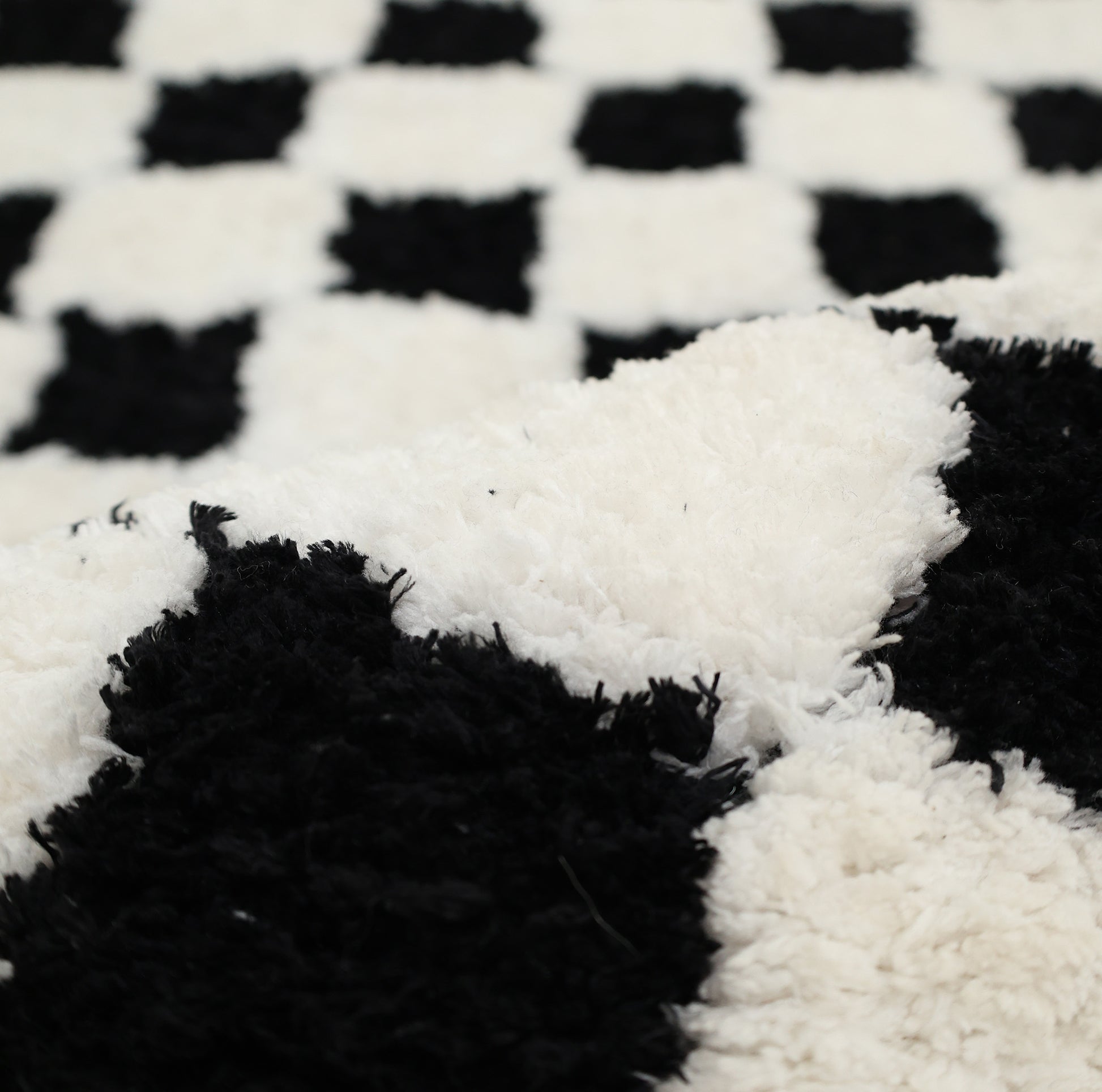 A close-up of the RAMSHA HOME Black & White Checkered Shaggy Rug (115x230 cm, SG-069) reveals its soft, textured fibers and slightly rumpled surface in the foreground.