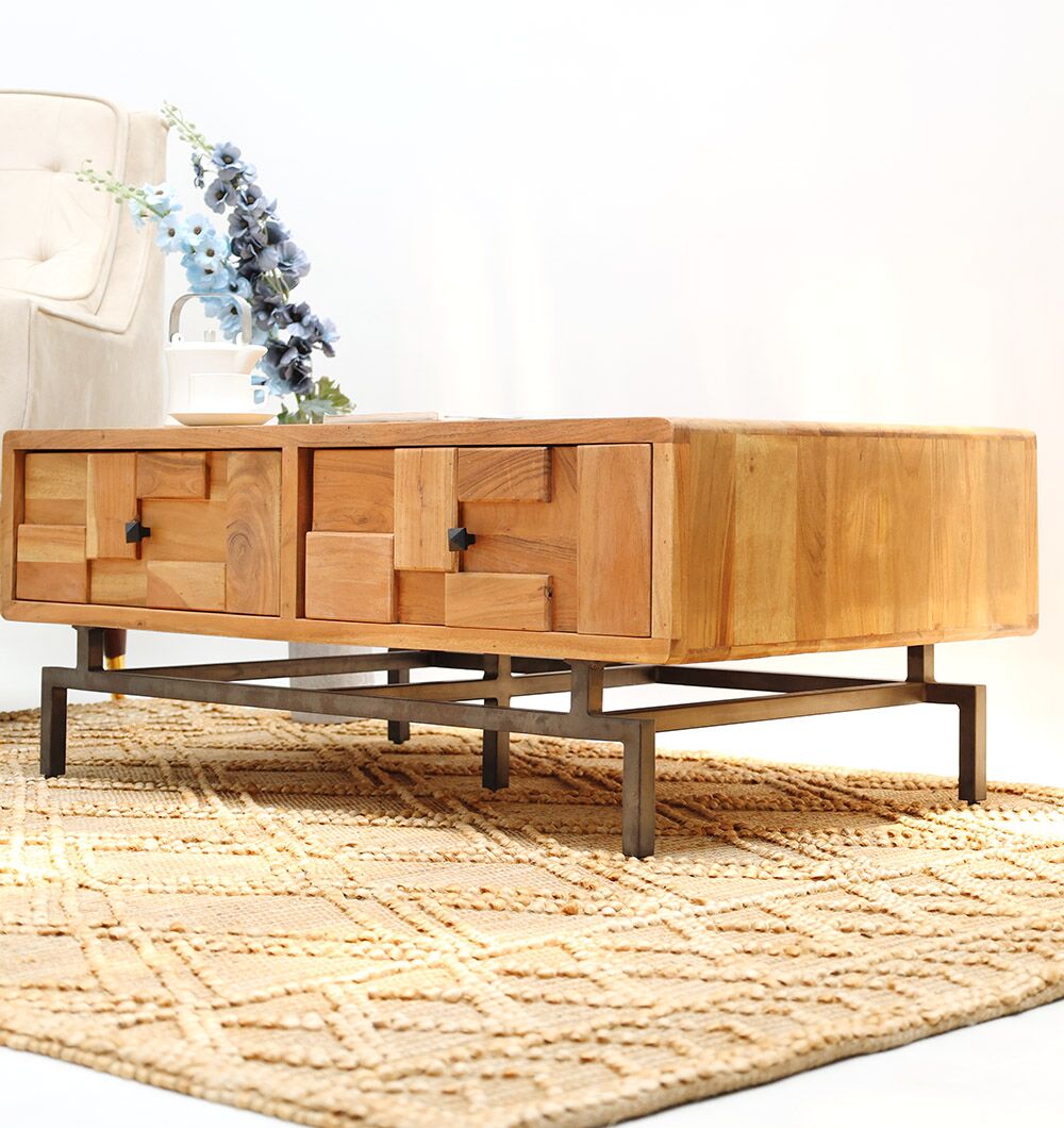 A wooden coffee table with a geometric paneled design and black metal legs sits on a textured beige rug. In the background, the RAMSHA HOME Modern Acacia Wood TV Cabinet with Metal Base and a cream armchair are partially visible.