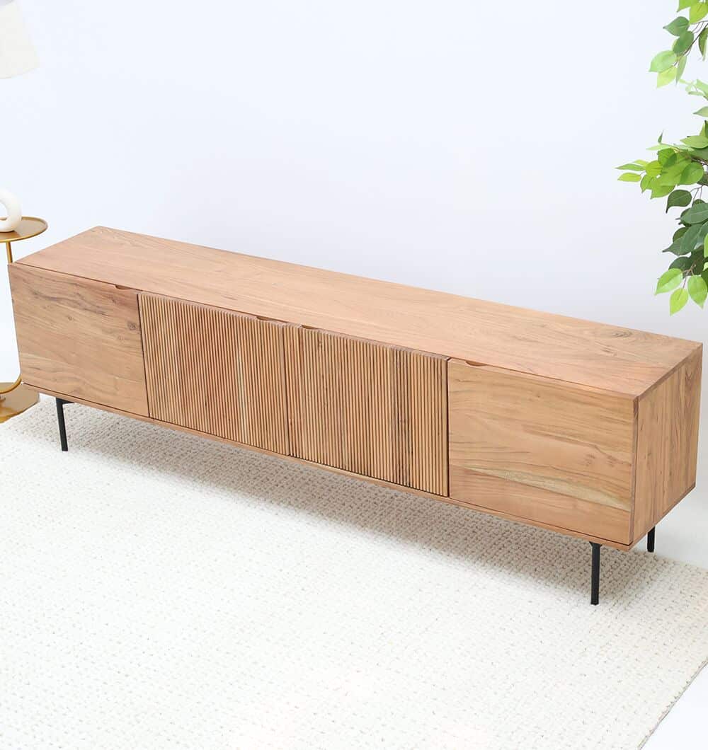 The RAMSHA HOME Wooden TV Cabinet with Storage features solid acacia construction, a metal base, and fluted panels. It sits on a light textured rug beside a leafy green plant, highlighting its modern, minimalist style.