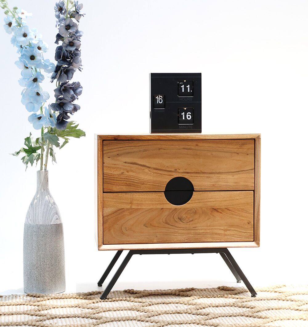 The RAMSHA HOME Solid Acacia Wood Sideboard Cabinet – 2 Drawer Storage Unit with angled black legs sits on a woven rug. A vase with blue and white flowers is on the left, and a black flip clock rests atop it against a white background.
